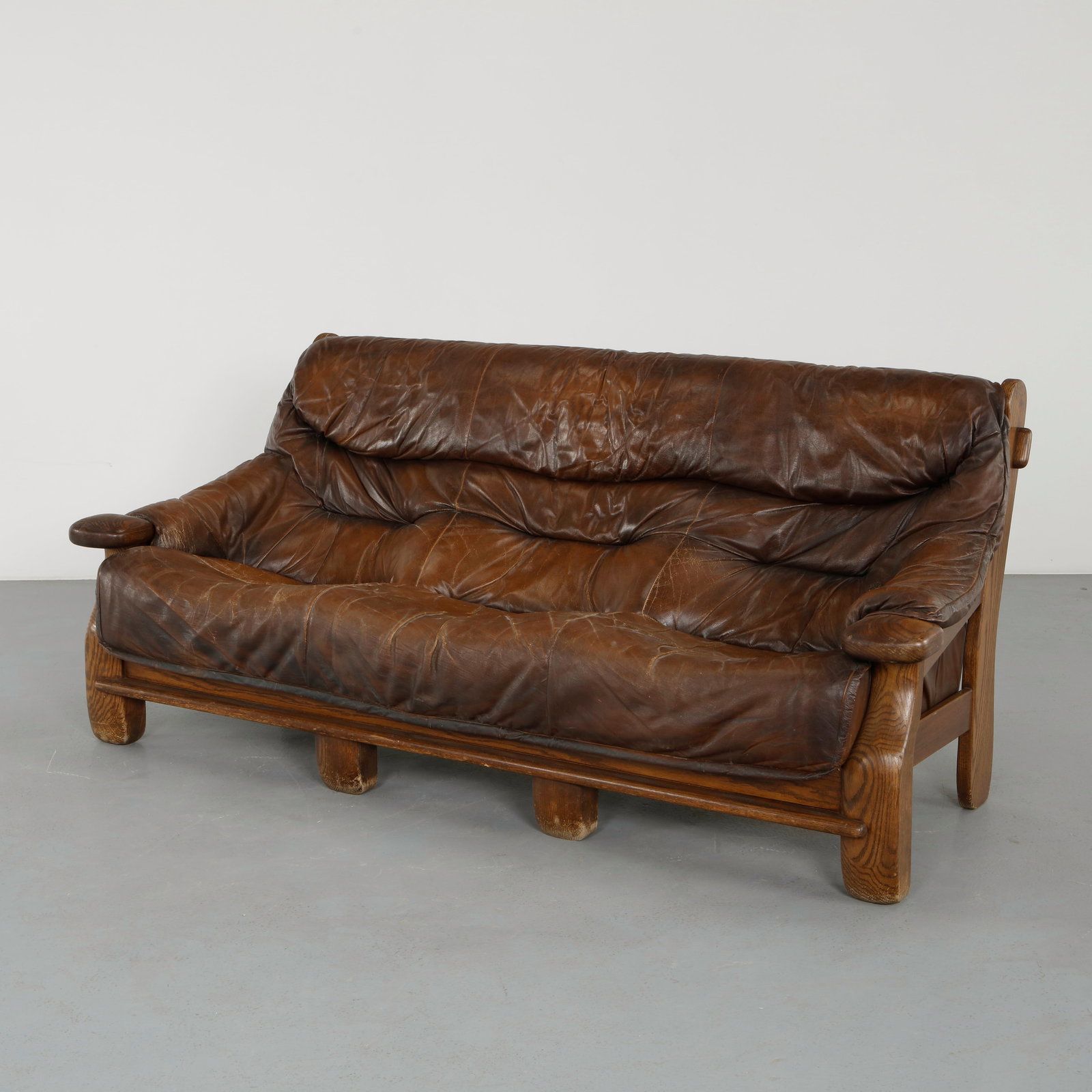 French Brutalist Leather Sofa, 1960s: A generous and inviting sofa featuring a solid wood frame with thick, patinated leather cushions. The supple upholstery displays a beautifully aged surface, enhancing its tactile appeal. A stunning an