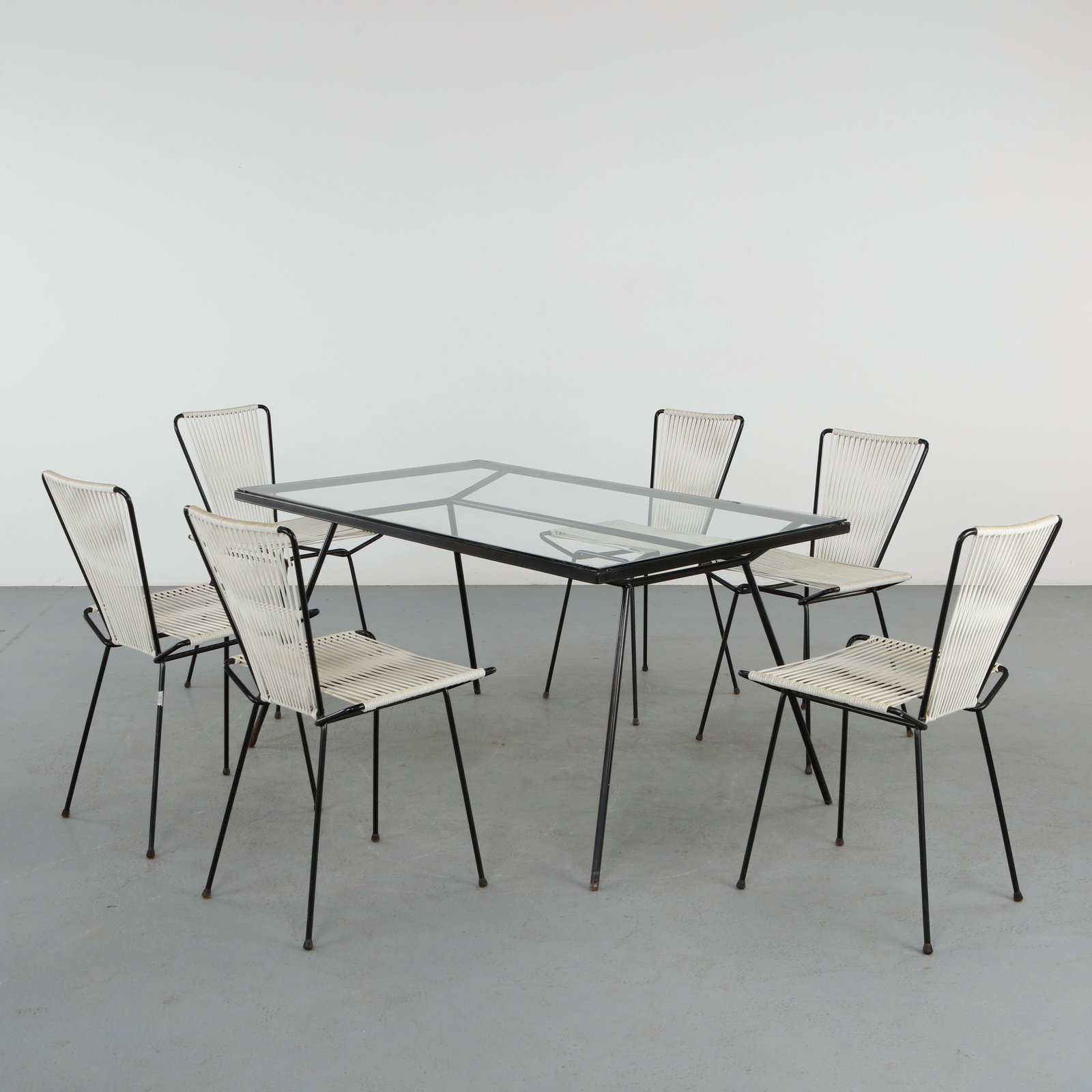 George Nelson Arbuck Wrought Iron Dining Table and Six Dining Chairs in the style of Allan Gould: Comprising a wrought iron base supporting a glass top, accompanied by chairs with graphic metal frames and woven seats. A balanced ensemble reflecting mid-century American design sensibilities. Table: