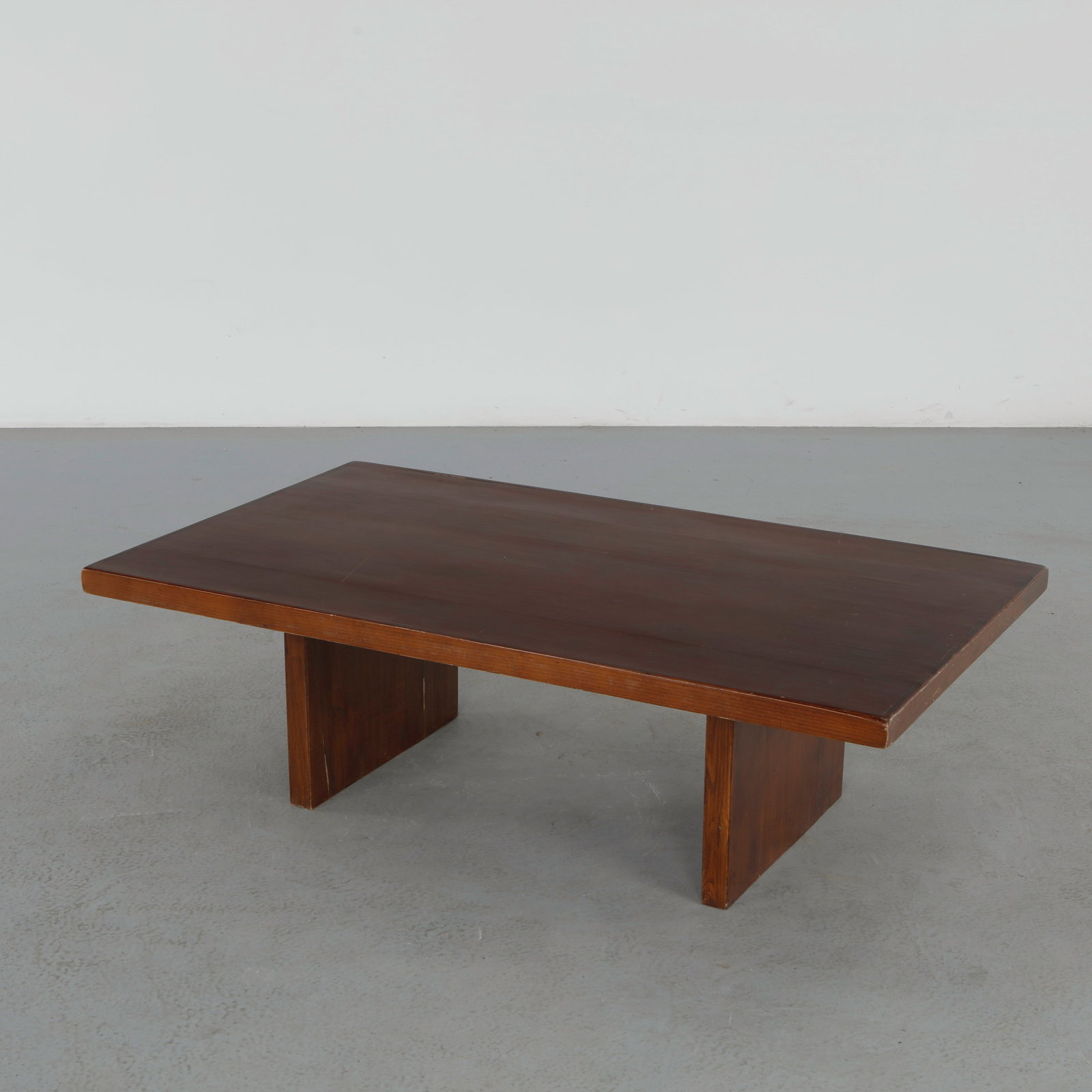 Brutalist Coffee Table attributed to Axel Vervoordt, 1980s: Minimalist low coffee table executed in richly toned wood with monolithic plank supports and refined geometric proportions. The restrained silhouette and architectural construction reflect the quiet s