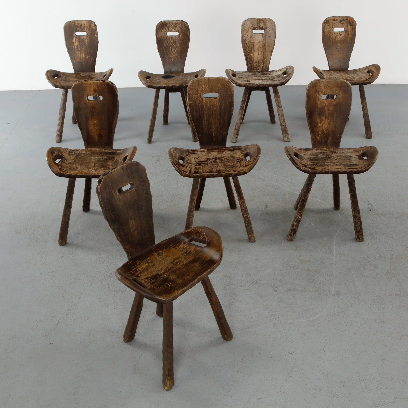 Set of Eight Brutalist Wood Chairs, 1950s: A rare suite of eight sculptural chairs crafted in solid wood, featuring thick slab seats and pierced backrests. The raw, timeworn surfaces and primitive joinery exemplify the brutalist aesthetic. A s