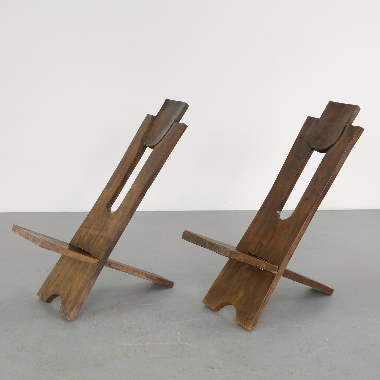 Pair of Brutalist West African Chairs, 1960s: Hand carved in solid wood, this chair embodies a sculptural Brutalist vocabulary defined by bold geometry and monolithic presence. The elongated backrest and carved seat reveal a raw, expressive appro