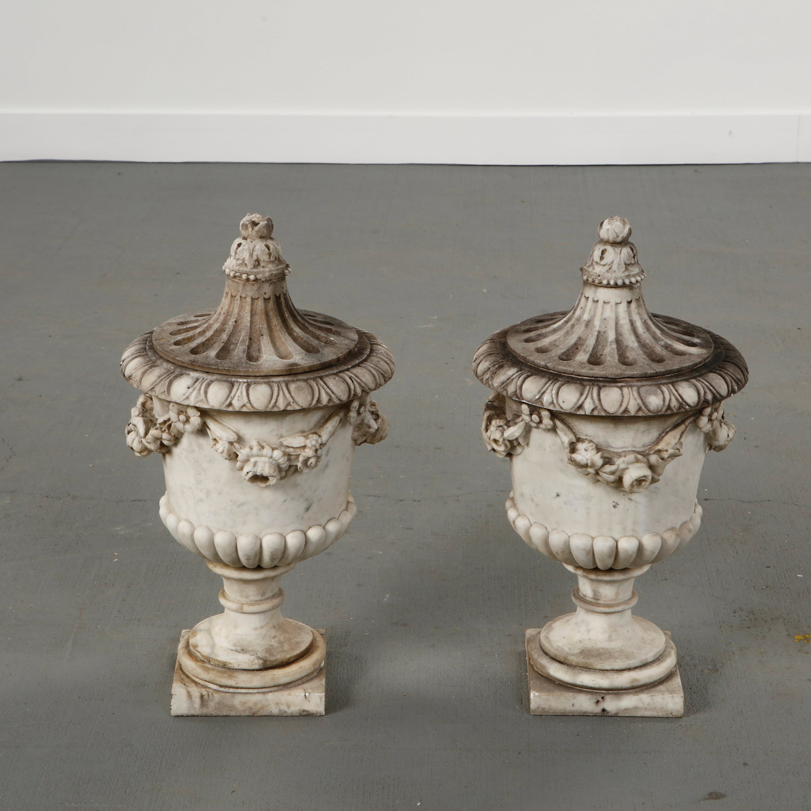Carrara Marble Castle Sculpture, France, 18th Century: Pair of carved Carrara marble urns with integral domed tops, featuring classical baluster forms, floral garlands and bead molding. Provenance from a French castle, with a richly weathered patina refle