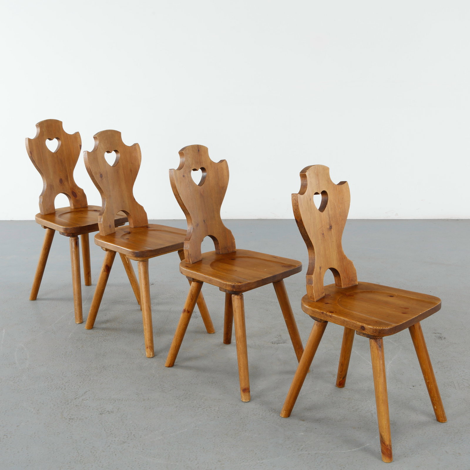 Set of Four Brutalist Folk Heart Back Dining Chairs, 1960s: Crafted in solid pine with carved heart motif backrests, these sculptural dining chairs embody the warmth and simplicity of Alpine folk craftsmanship. Their tapered legs and softly rounded forms