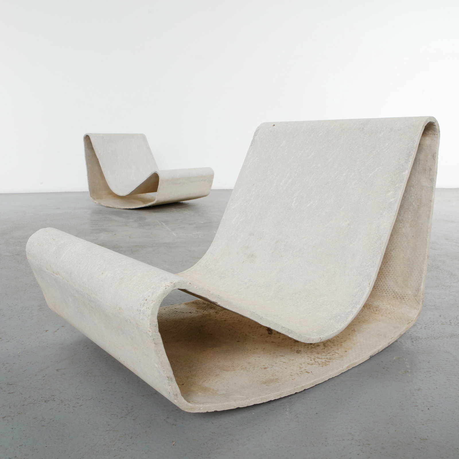 Willy Guhl, Pair of Loop Chairs, 1960s: A striking pair of sculptural lounge chairs crafted from fiberconcrete with a weathered patina. The minimalist, curved design enhances their brutalist aesthetic, making them ideal for indoor or outdoo