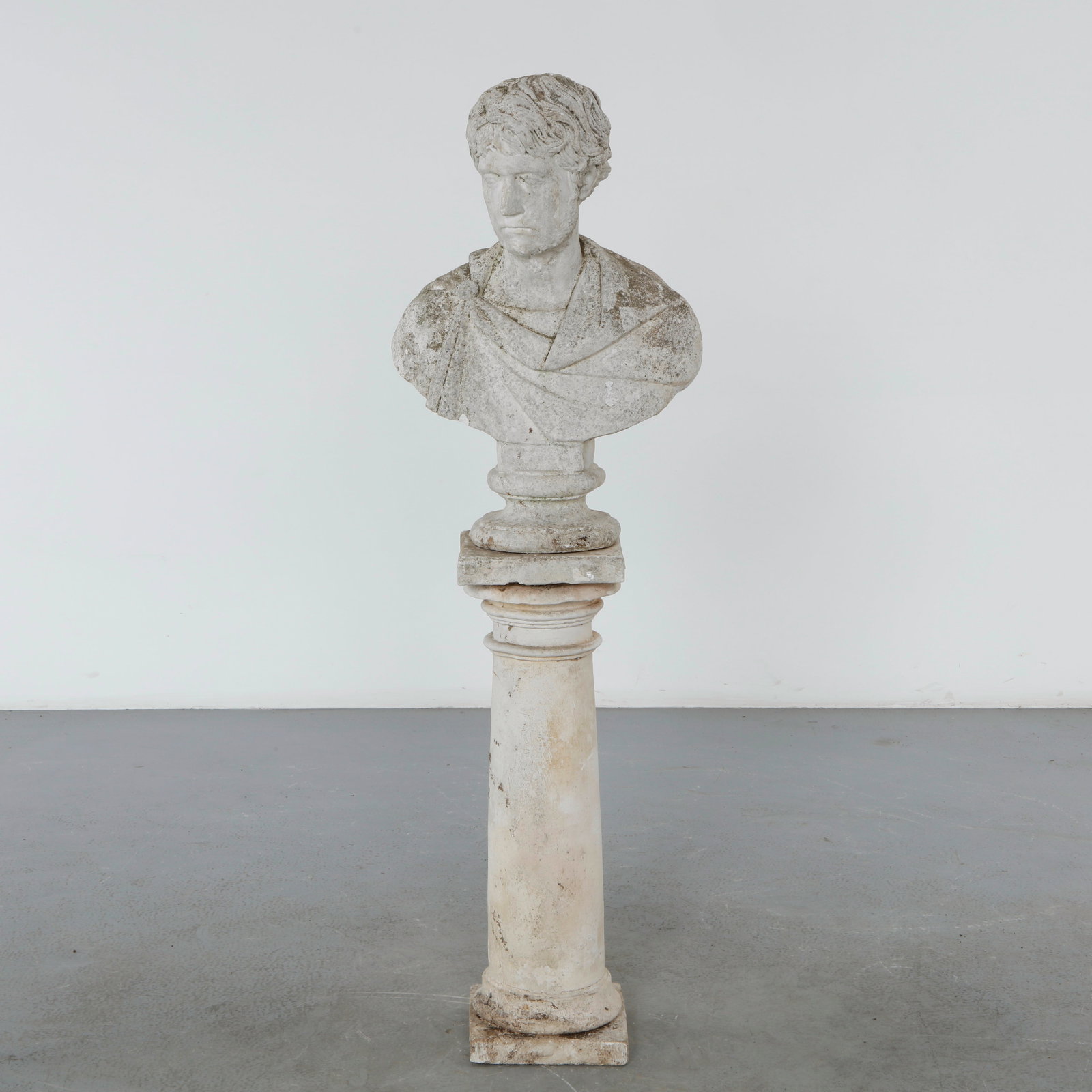 Limestone Statue on Stand, 1960s: A classical-inspired limestone bust depicting a young figure, raised on a substantial pedestal. The weathered surface and sculptural detailing lend the piece a timeless presence, equally suited to