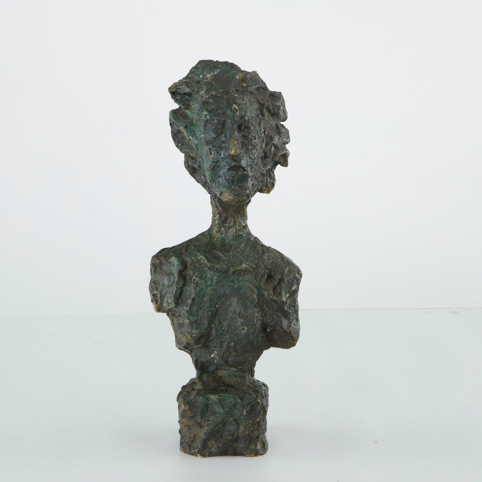 Textured Bronze Bust of a Woman attributed to A. Giacometti, Numbered 21/30: A textured bronze bust depicting a stylized female figure, with an elongated head and shoulders rising from a rough-hewn, sculptural base. The heavily worked surface, with its pitted, irregular textur