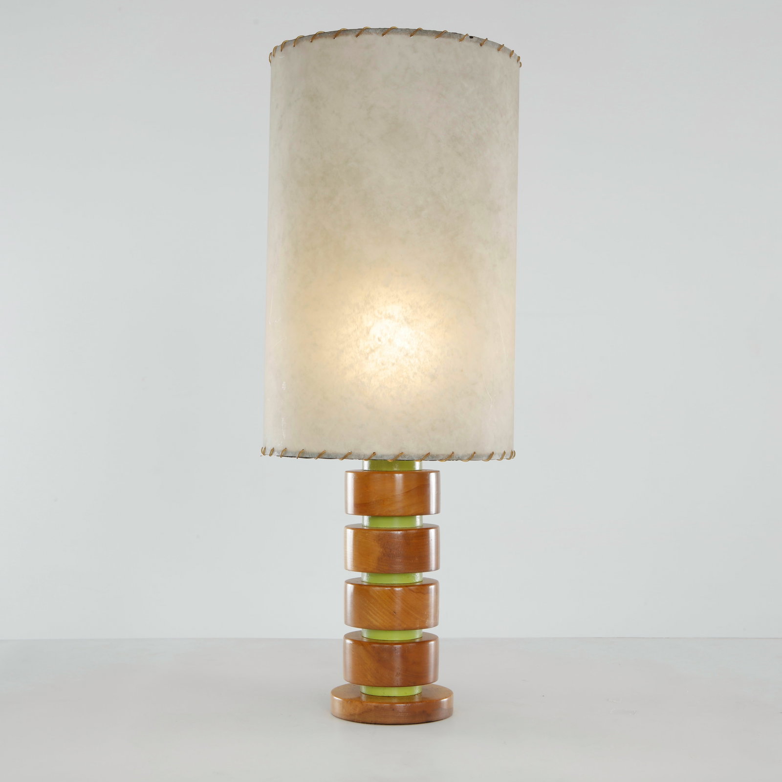 Stacked Turned Wood Table Lamp, Italy, 1970s: The base formed of graduated turned wood discs alternating with green-lacquered spacers, fitted with a laced parchment-style shade with whipstitched brass-wire edge. Warm honey patina to the wood.