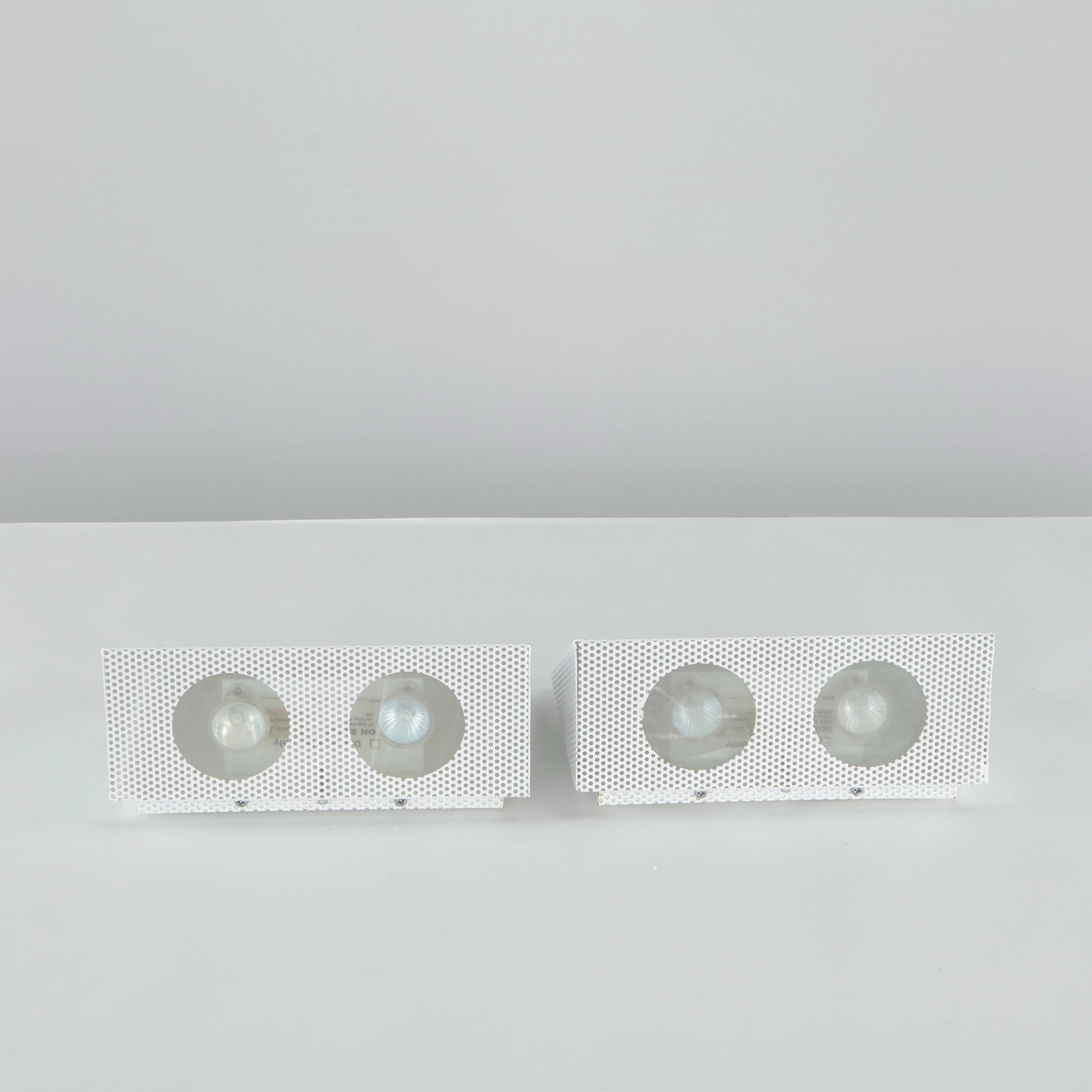 Ron Rezek, Pair of Postmodern Wall Sconces, 1970s: White powder-coated perforated metal in a triangular form with frosted glass diffusers. Labeled Ron Rezek, UL listed. Wiring not verified. Height: 4.5 in. Length: 9.25 in. Width: 8.5 in.