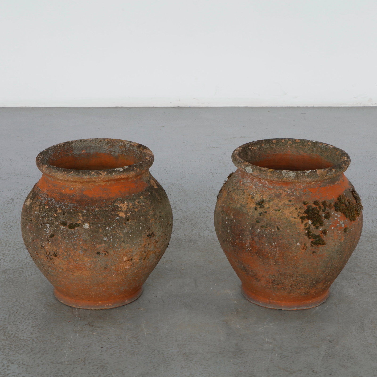 Pair of Ceramic Olive Jar Planters, 1960s: A decorative pair of terracotta olive jar planters featuring weathered surfaces and rich natural patina acquired through outdoor use. Their generous proportions and Mediterranean character make them i