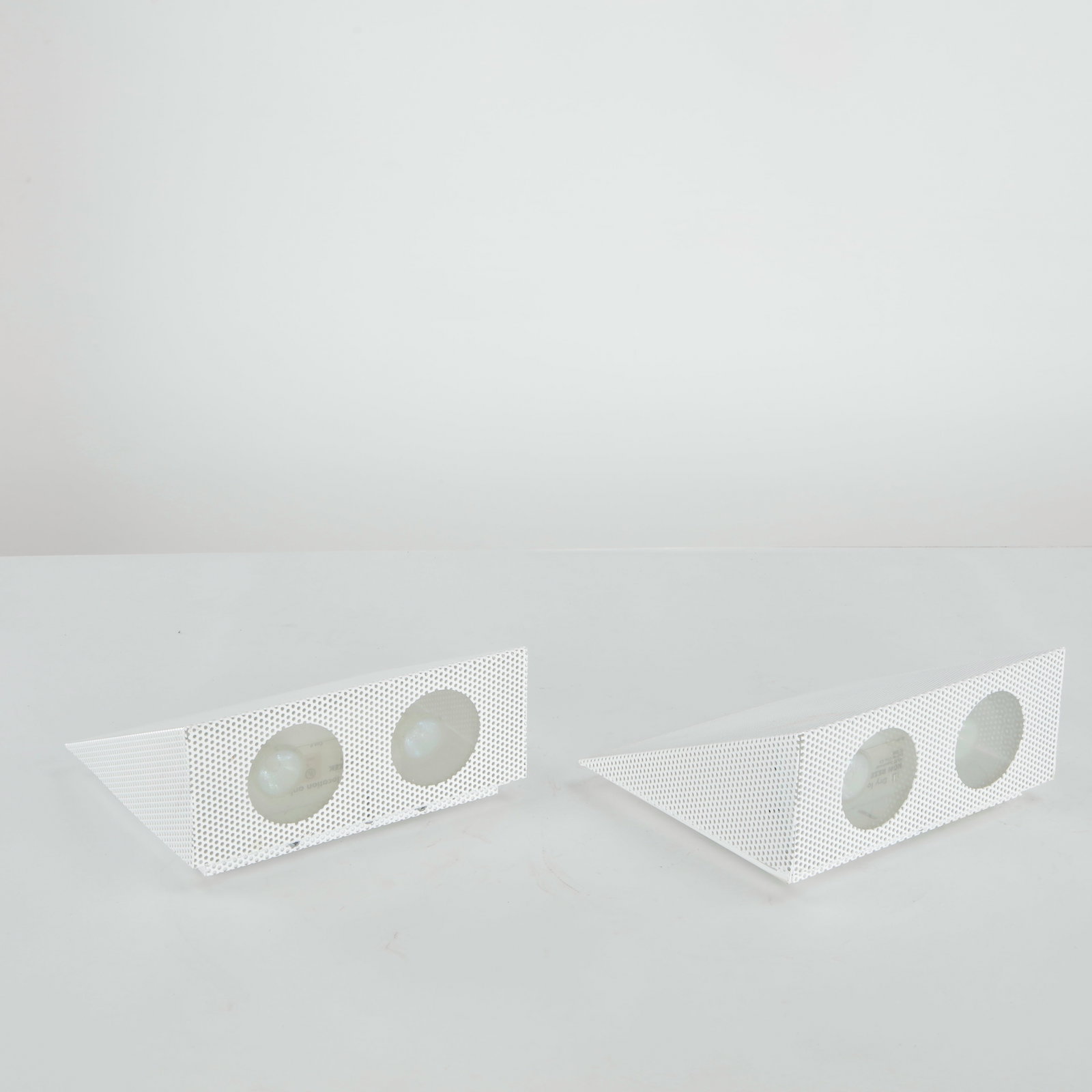 Ron Rezek, Pair of Postmodern Wall Sconces, 1970s: White powder-coated perforated metal in a triangular form with frosted glass diffusers. Labeled Ron Rezek, UL listed. Wiring not verified. Height: 4.5 in. Length: 9.25 in. Width: 8.5 in.