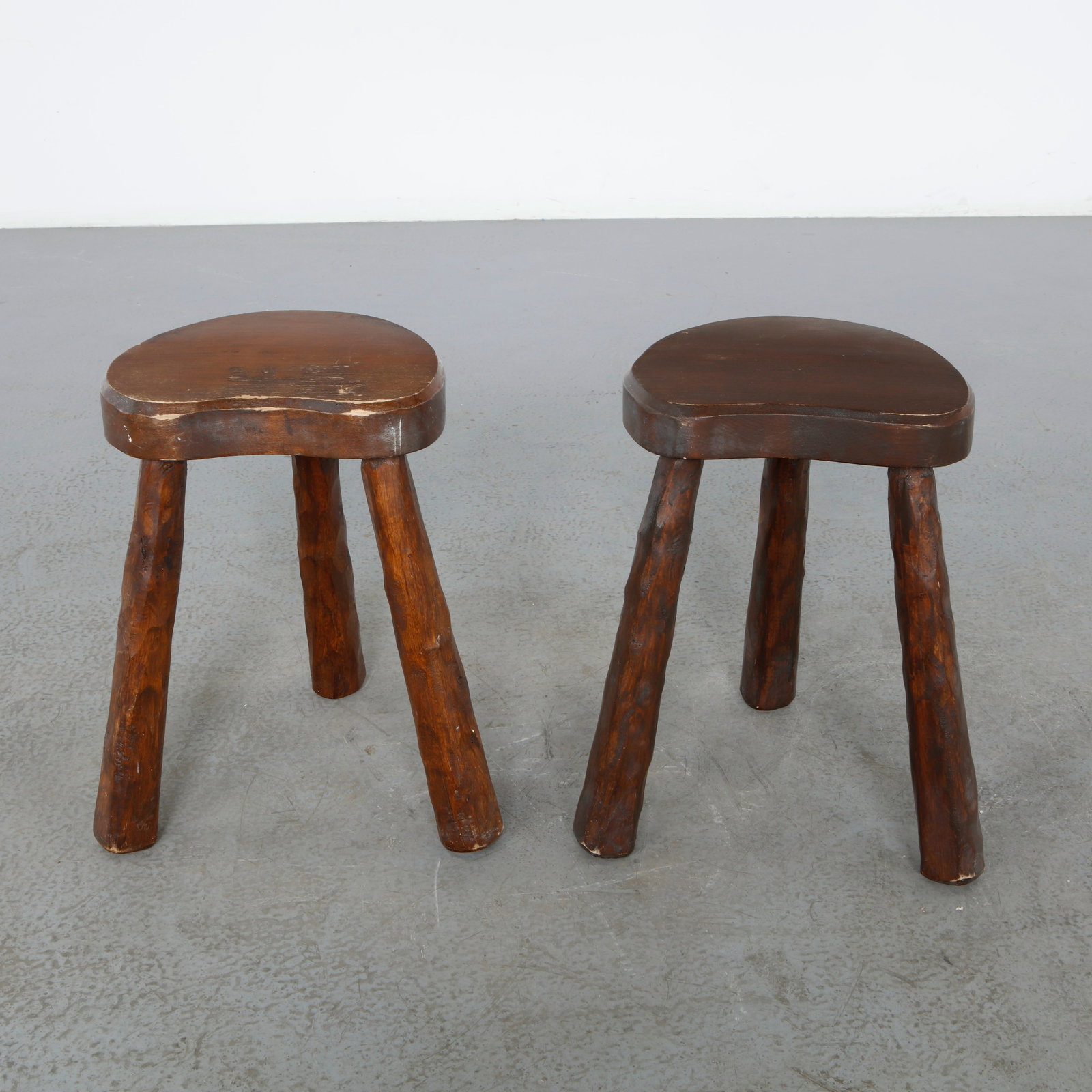 Pair of Rustic Tripod Stools, France, 1960s: A sculptural pair of handcrafted solid wood tripod stools, featuring organic forms and a richly patinated finish. Their primitive character and robust construction make them timeless examples of rusti