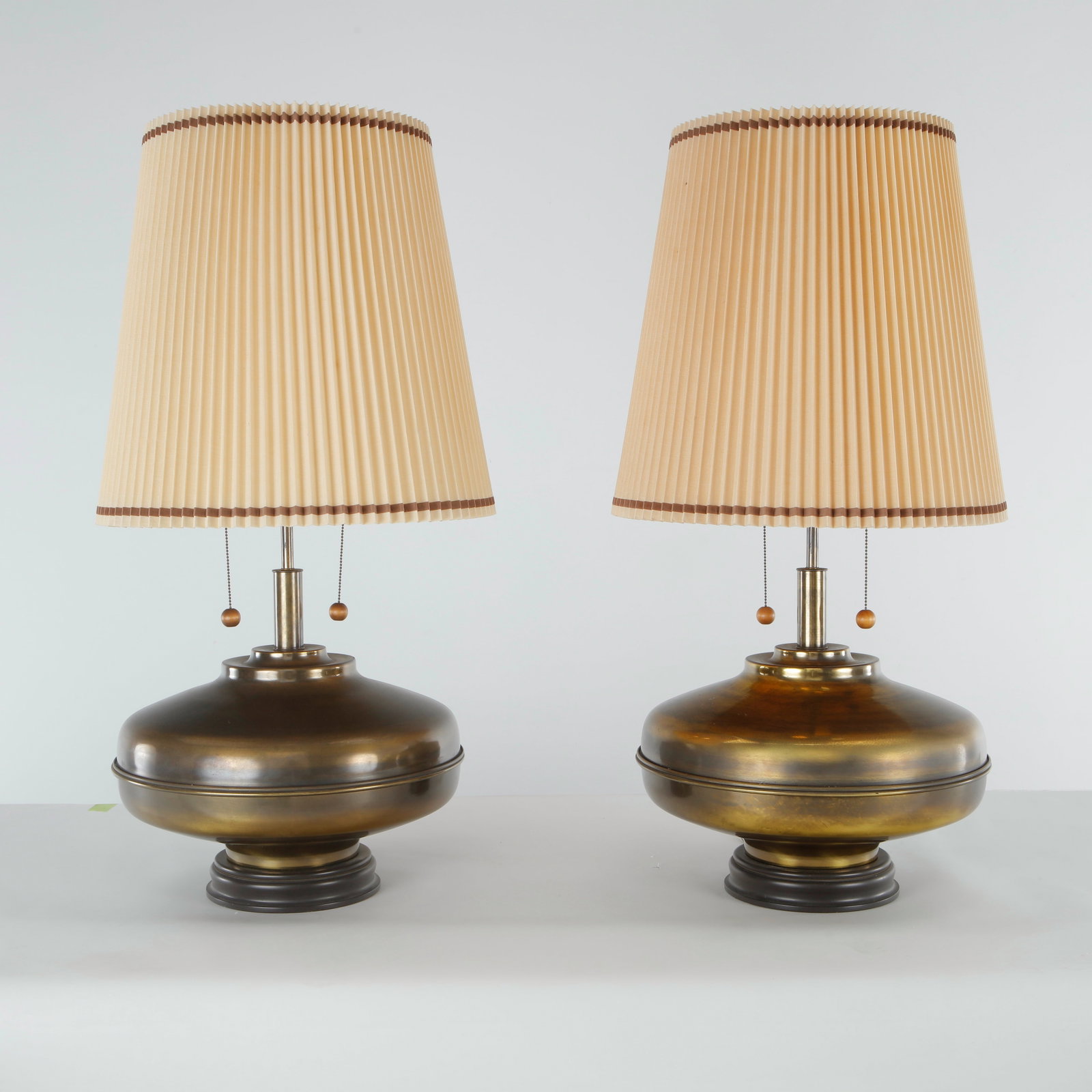 Marbro, Pair of Mid-century Polished Brass Table Lamps, 1960s: A pair of substantial mid-century table lamps by Marbro, with bulbous polished brass bodies raised on ebonized wood bases. Each fitted with dual sockets and pull-chain switches, and topped with a plea