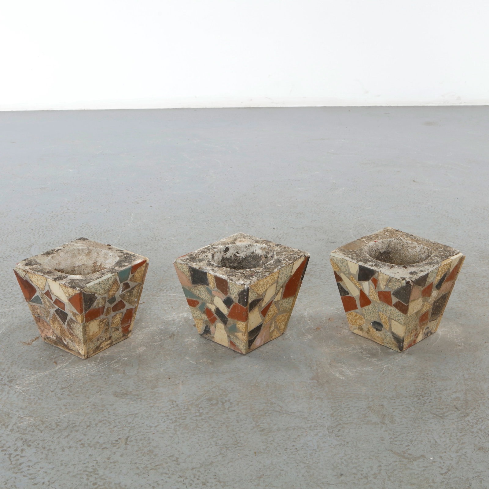 Set of Three Mosaic Concrete Planters, 1960s: Striking set of three handcrafted concrete planters featuring colorful terrazzo-style ceramic mosaic cladding in a geometric composition. Their sculptural tapered form and richly textured surfaces