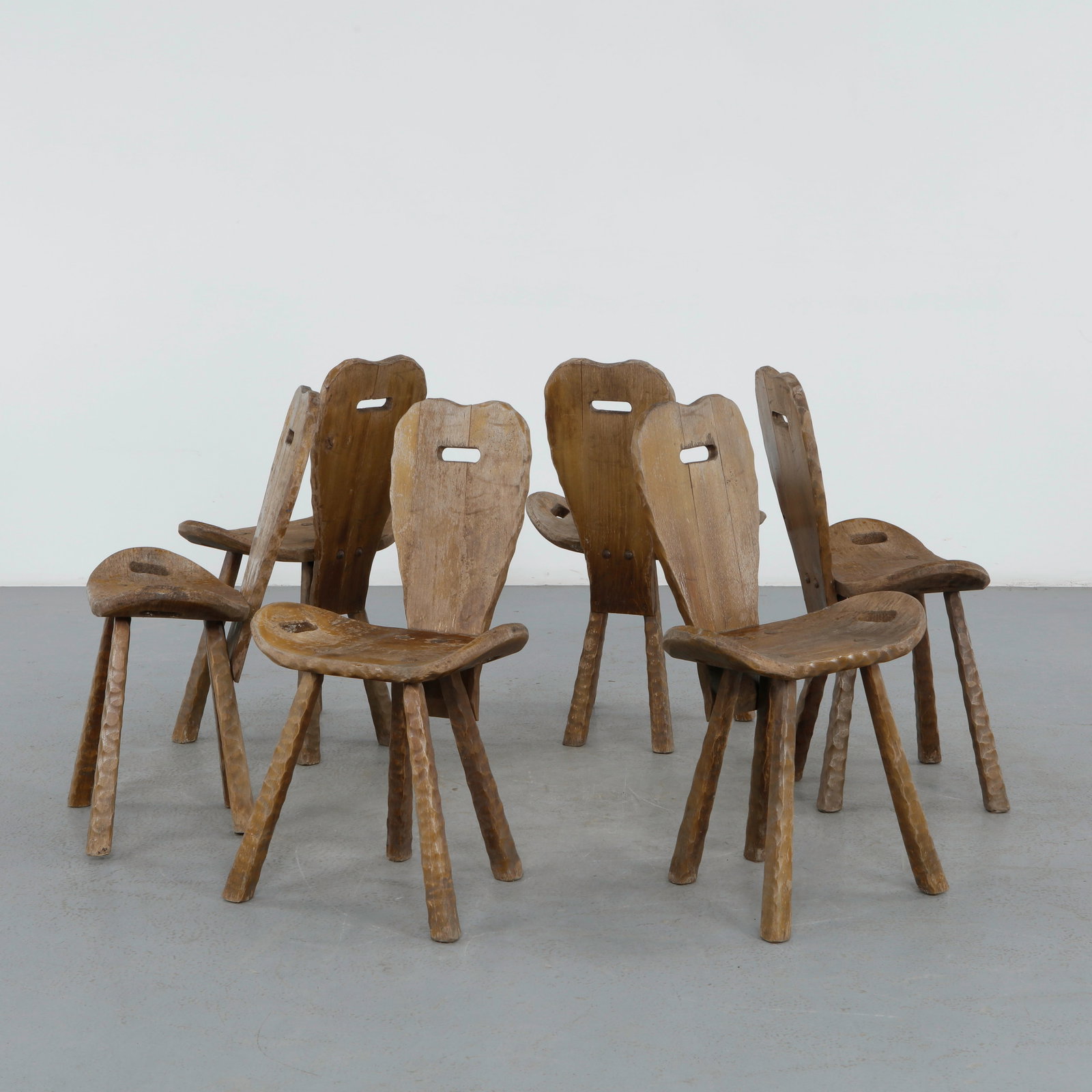 Set of Six Brutalist Wood Chairs, 1950s: A rare suite of four sculptural chairs crafted in solid wood, featuring thick slab seats and pierced backrests. The raw, timeworn surfaces and primitive joinery exemplify the brutalist aesthetic. A
