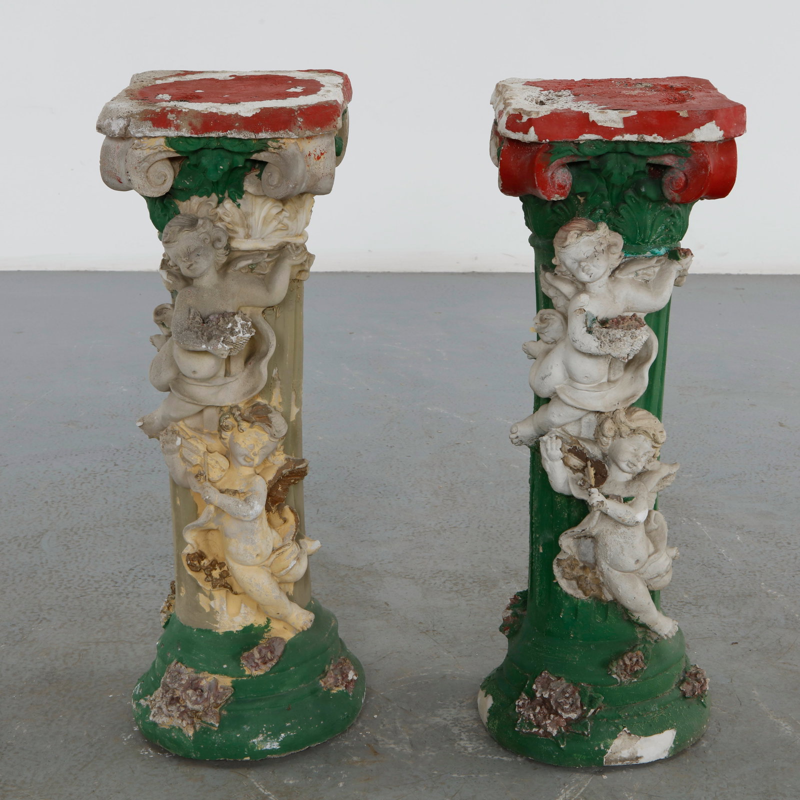 Pair of Decorative Erated Concrete Garden Pedestals with Cherub Reliefs, 1970s: Executed in painted aerated concrete, this pair of garden pedestals features richly modeled Corinthian capitals adorned with sculptural cherubs and floral garlands. Their weathered polychrome finish