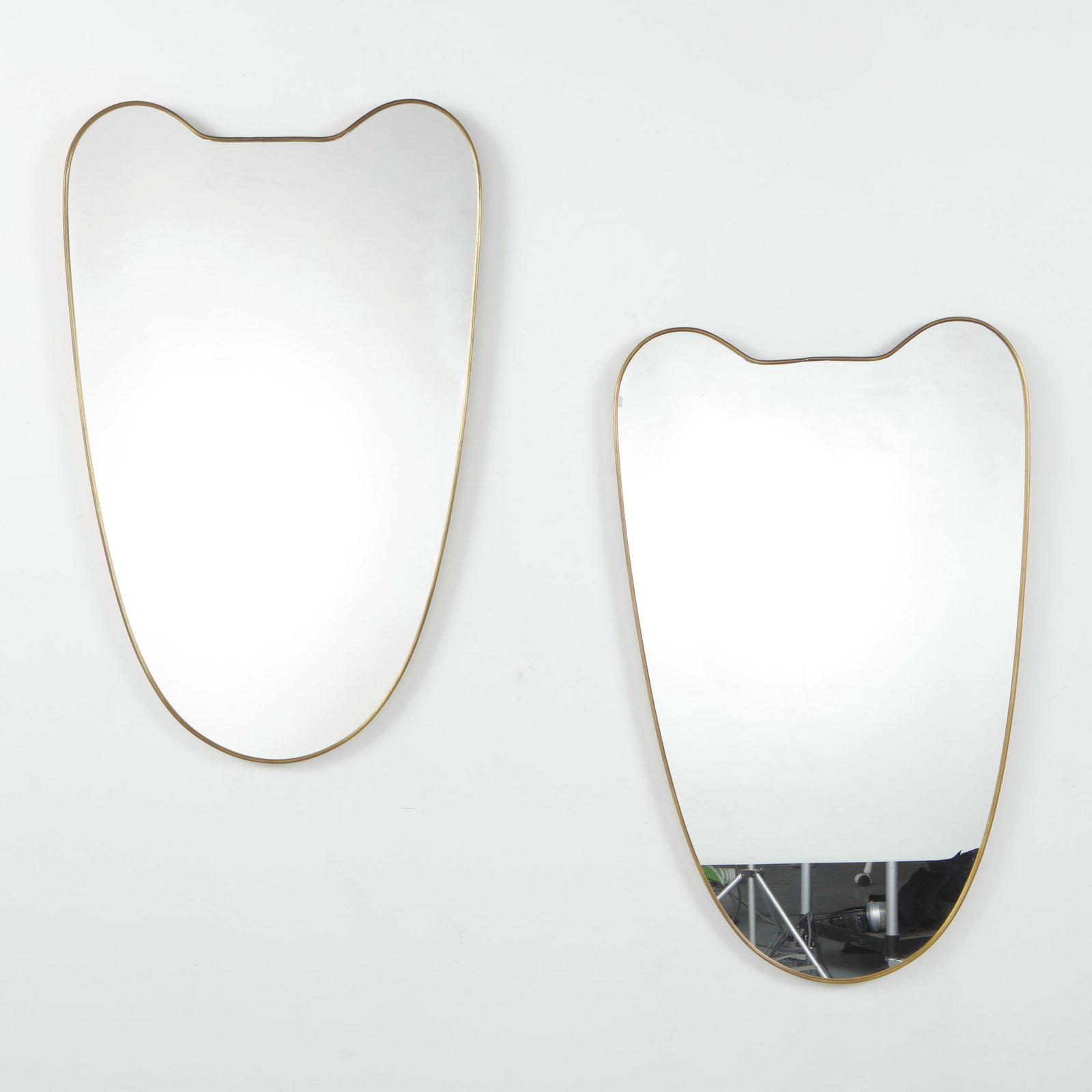 Pair of Italian Brass Mirrors, Notched Shield Form, 1950s: A pair of Italian mid-century mirrors with slender brass frames, in an organic shield form with a distinctive notched top edge. Height: 41 in. Length: 25 in. Width: 1.5 in.
