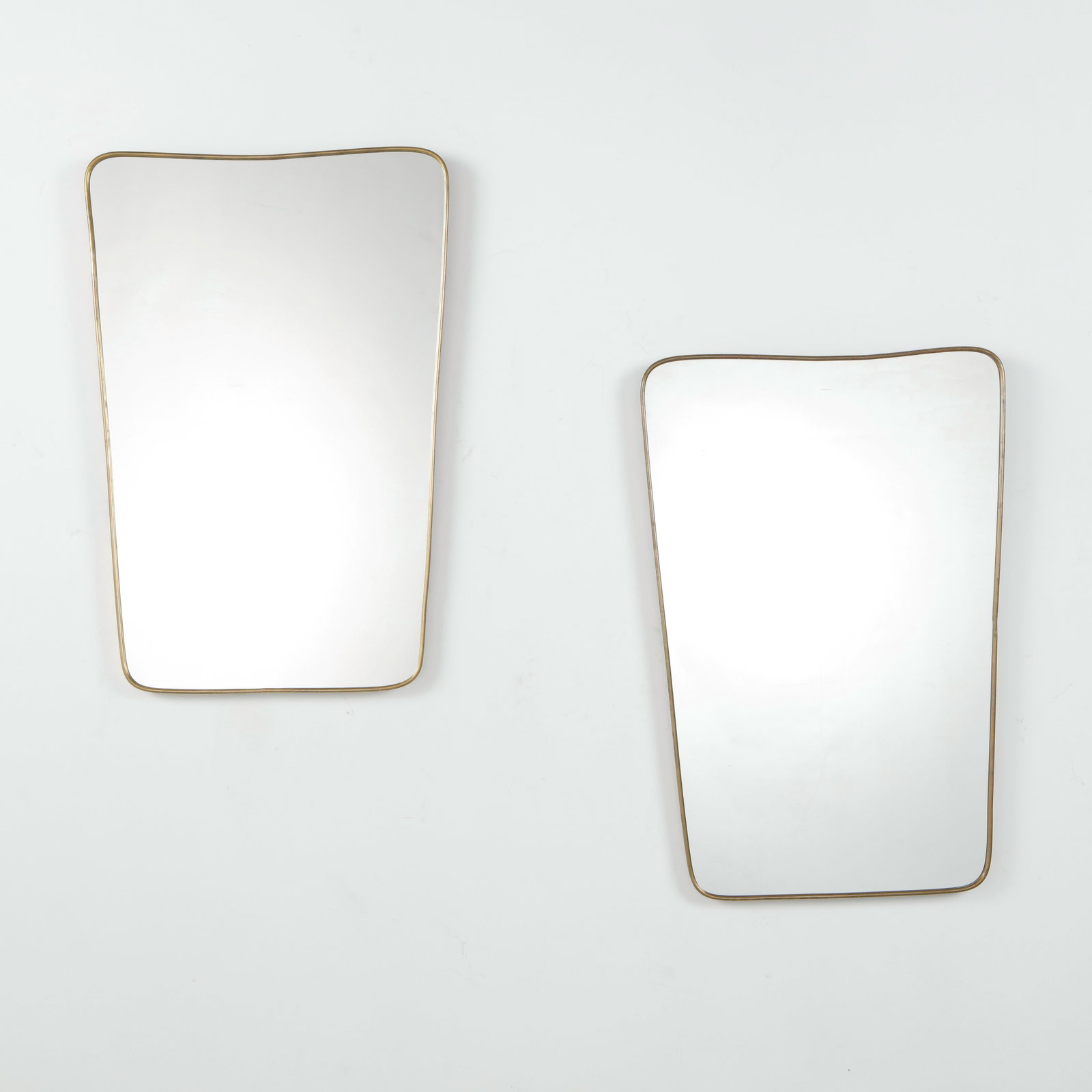 Pair of Italian Brass Mirrors, Asymmetric Wave Form, 1950s: A pair of Italian mid-century mirrors with slender brass frames, in a tapering rectangular form with an asymmetric wave-shaped top edge. Height: 32 in. Length: 21.5 in. Width: in.