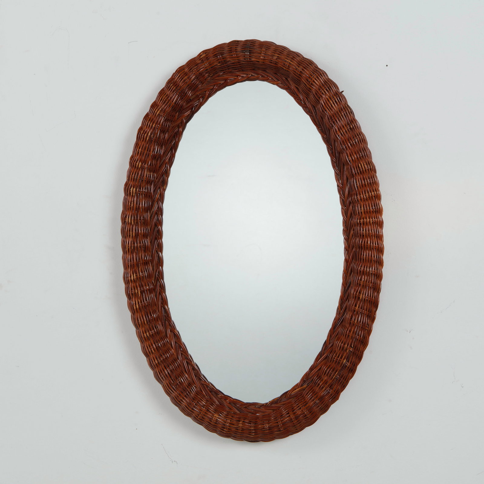 Audoux Minet, Woven Wicker Oval Mirror, Mid-Century: An oval mirror encircled by a thick, tightly woven wicker frame, in a warm brown tone. Height: 28 in. Length: 19 in. Width: in.