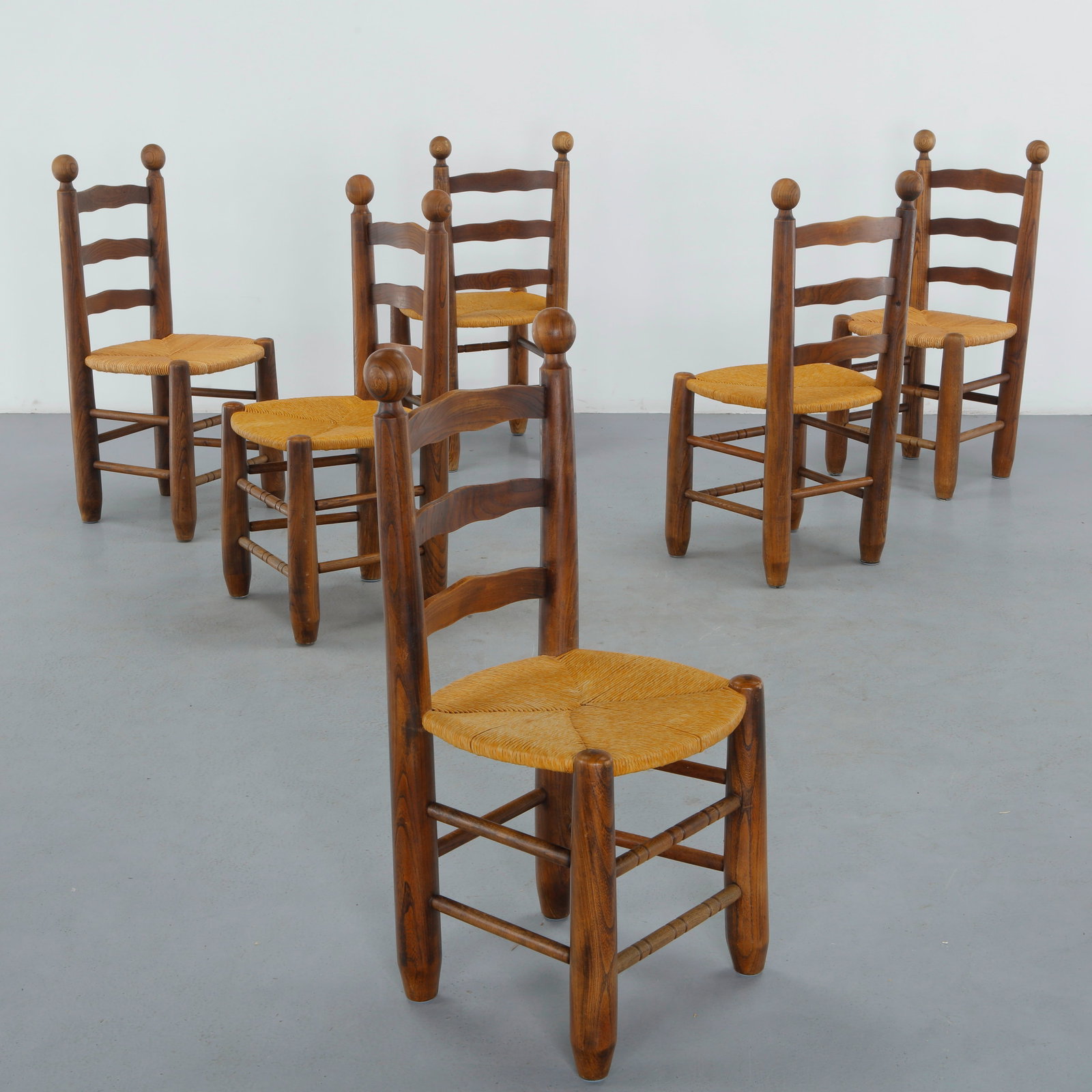 Charles Dudouyt, Set of Six Wood and Rope Chairs, 1950s: Six French dining chairs by Charles Dudouyt in dark stained oak, with ladder backs topped by turned ball finials, with woven rush seats, a rustic-chic design characteristic of Dudouyt mid-century work