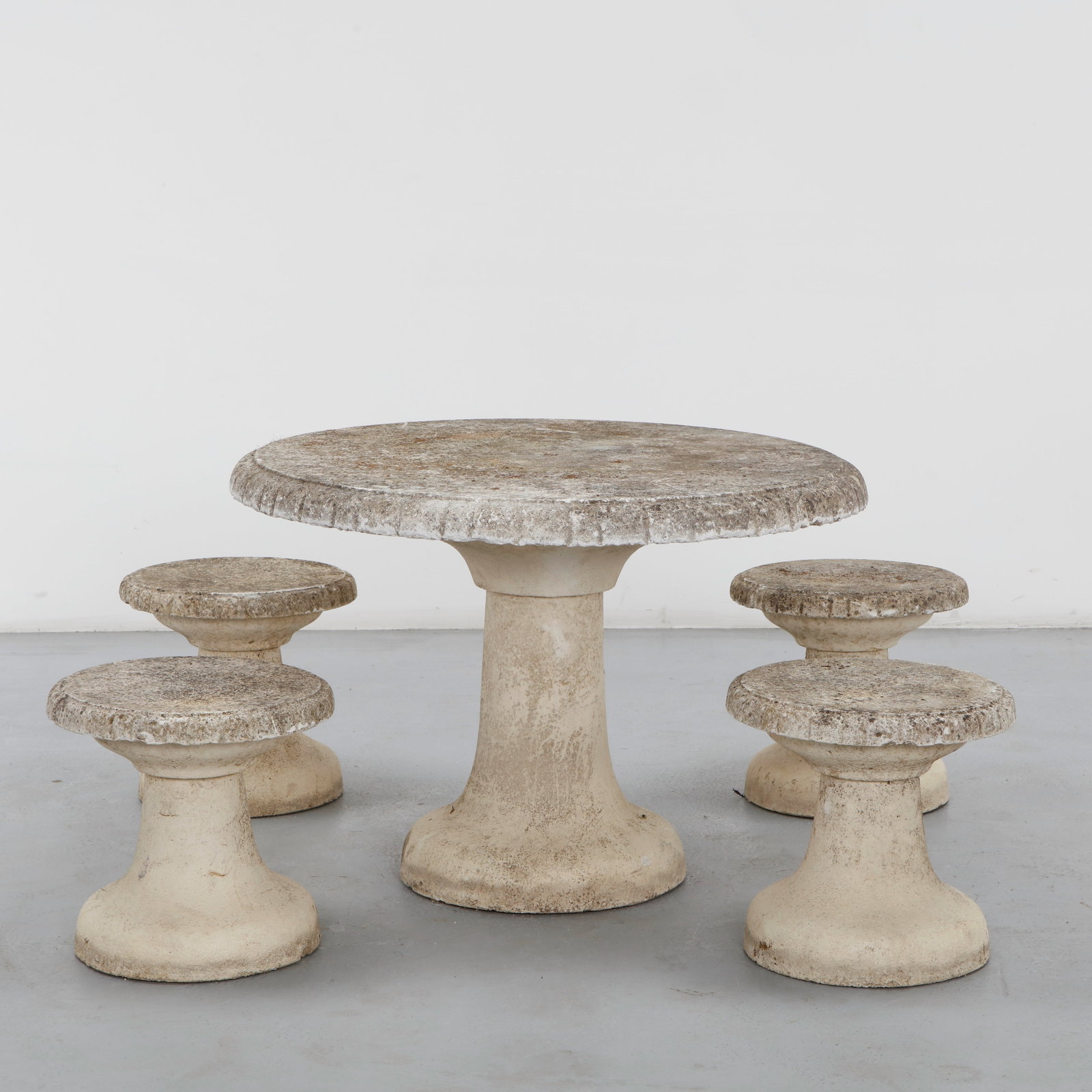Angelo Mangiarotti, Stone Outdoor Garden Set, 1960s: A weathered concrete garden ensemble comprising a round table with a scalloped edge on a trumpet-shaped pedestal, and four matching stools in the same hourglass silhouette, all showing an attractive a
