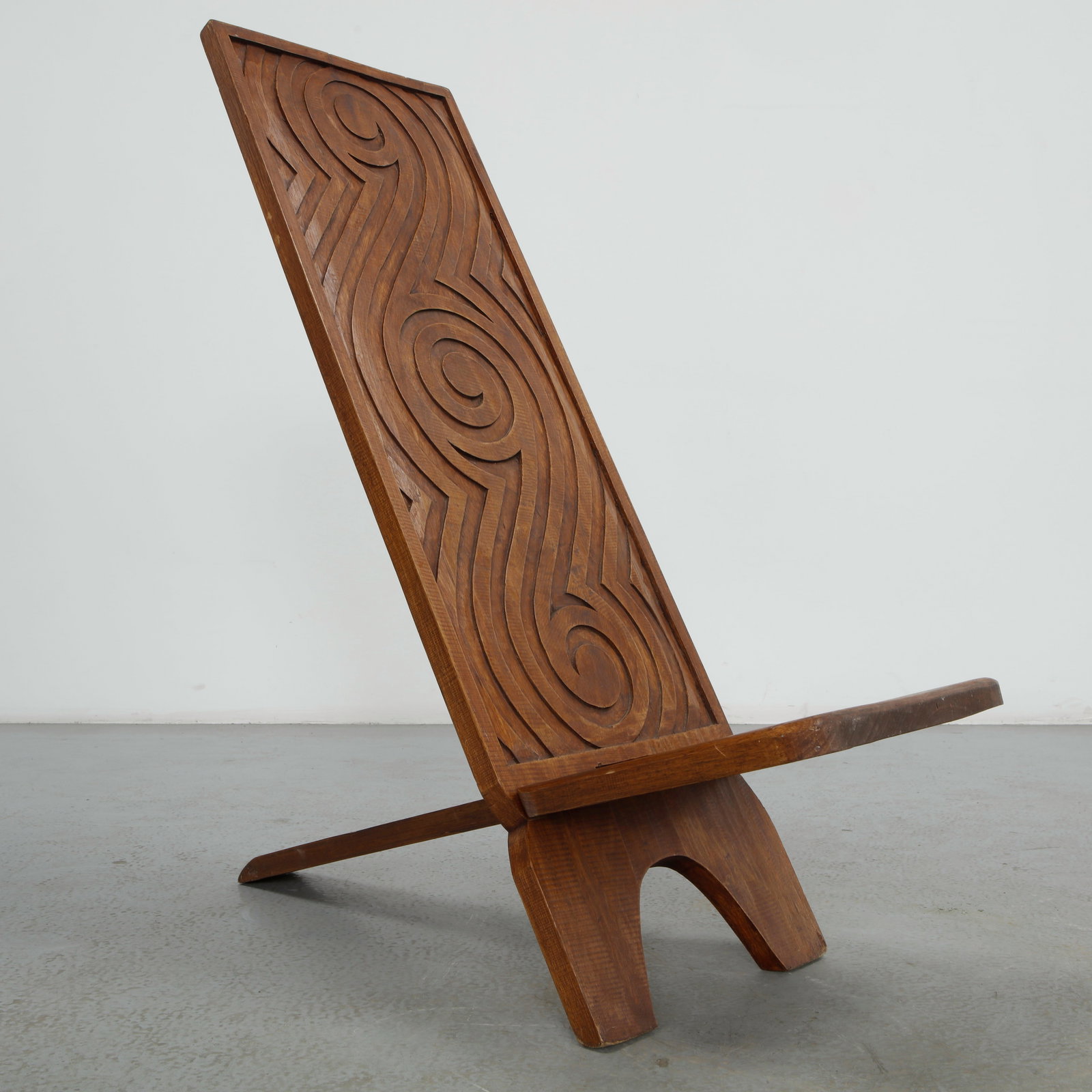 Hand-Carved African Folding Chair: Hand carved from solid wood, this folding chair combines a tall back panel carved with a bold spiral motif and a flat seat, joined by a pivoting hinge and supported by a single raking leg with a shape