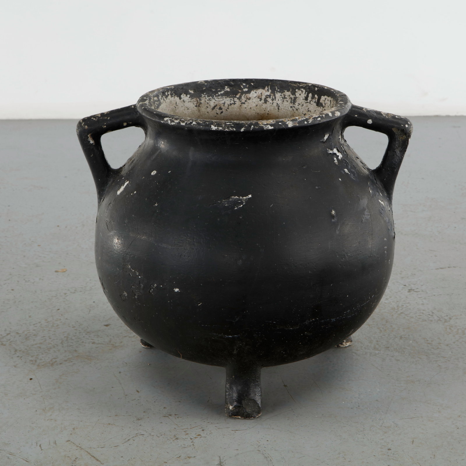 Willy Guhl, Black Cauldron Planter, 1960s: Executed in fiber cement, this cauldron form planter features two loop handles and raised tripod feet beneath a black painted finish. Losses to the surface reveal the pale material beneath, adding tex