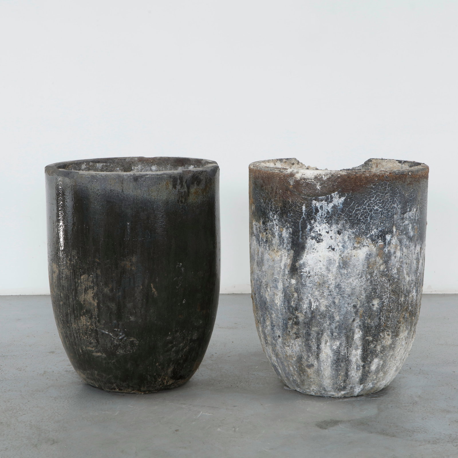Pair of Large Foundry Crucible Planters, 1960s: Industrial cast planters with softly tapered cylindrical bodies and a richly aged surface. Layers of oxidation and mineral patina create a complex tonal variation across the metal. Robust and understa