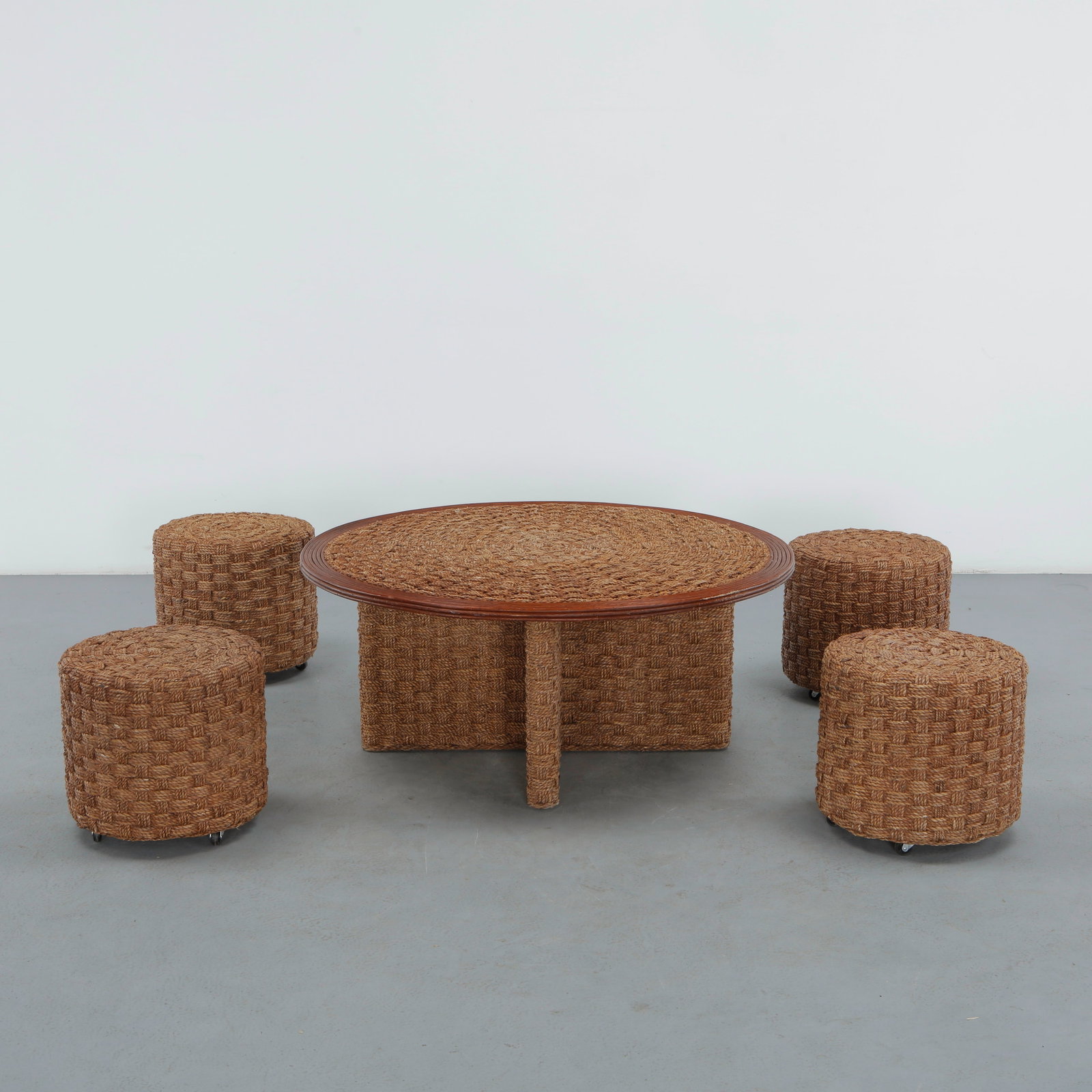 Organic Low Table with Four Handwoven Stools in the Style of Audoux Minet, 1960s: A round low table with a wood rimmed top hand woven in rope, resting on a cross form base entirely wrapped in the same basket-woven rope, accompanied by four cylindrical stools on castors, similarly h