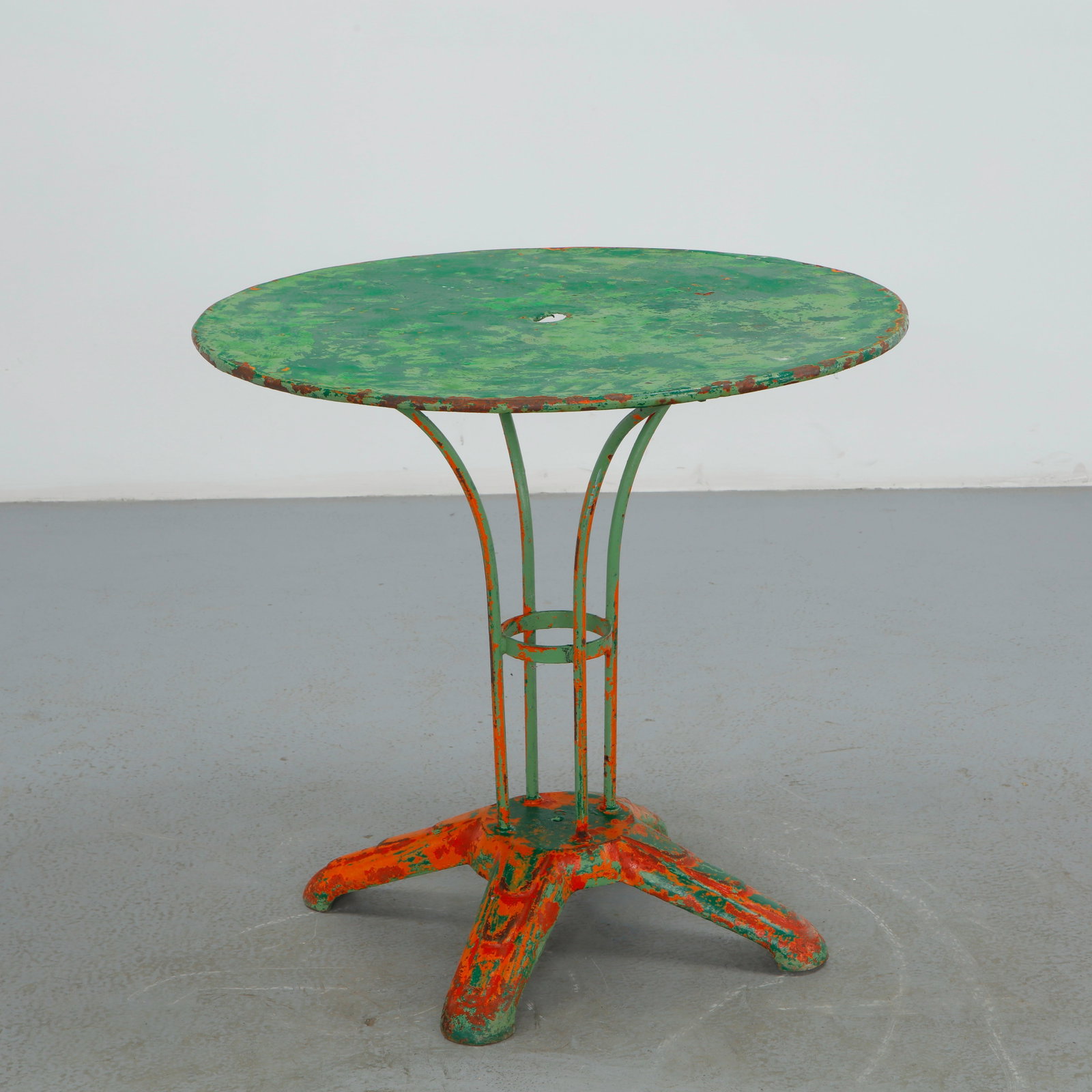 Round Parisian Metal Garden Table, 1950s: Constructed from painted metal, this round garden table is raised on a four legged base with a central umbrella ring. The heavily weathered surface, with losses revealing layers of paint, lends a rich