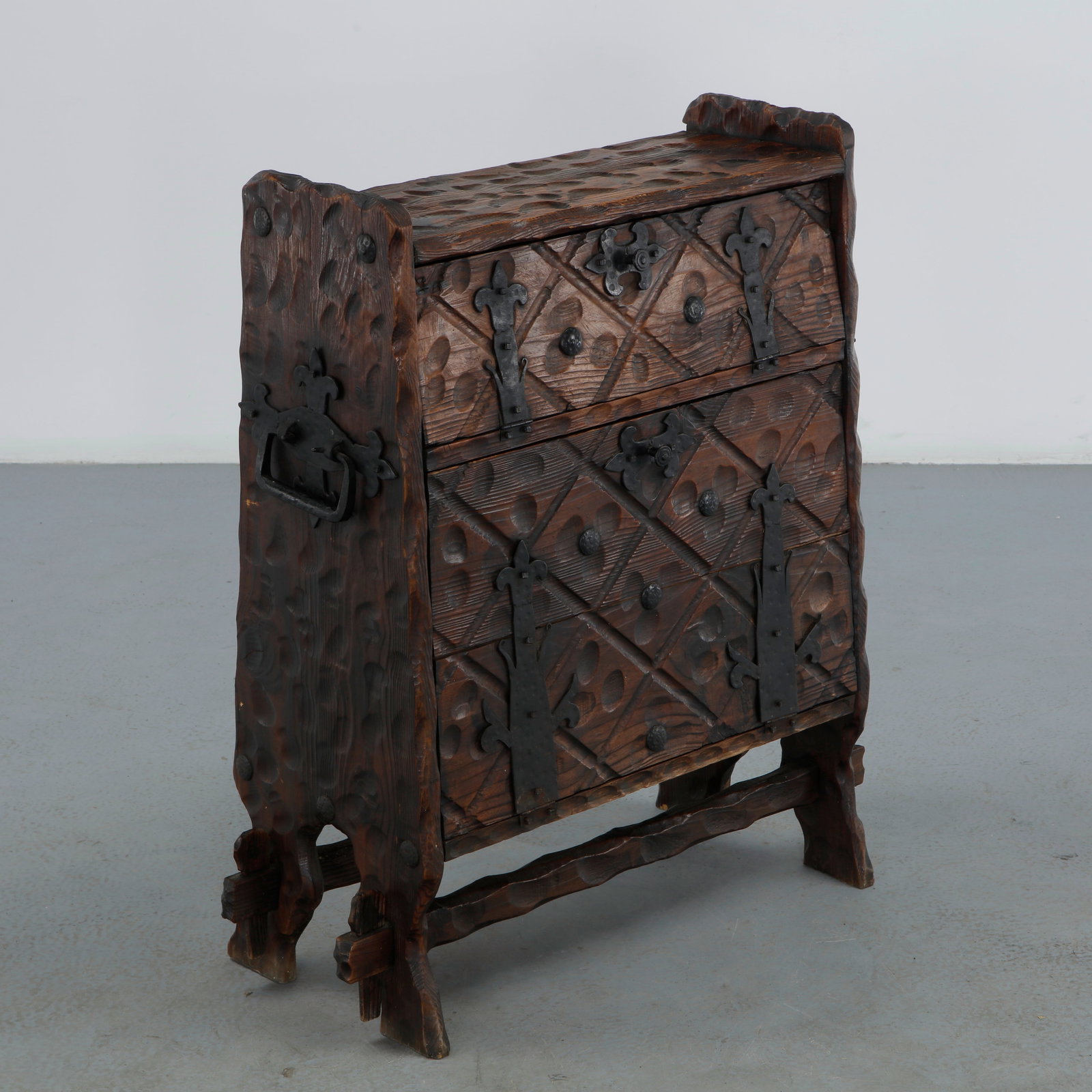 Brutalist Hand Carved Sideboard in the style of Ateliers Marolles, 1950s: A brutalist sideboard in dark stained wood, its surfaces deeply gouge carved in an organic dimpled texture and further decorated with wrought iron fleur de lis straps and a sculptural iron handle. Rai