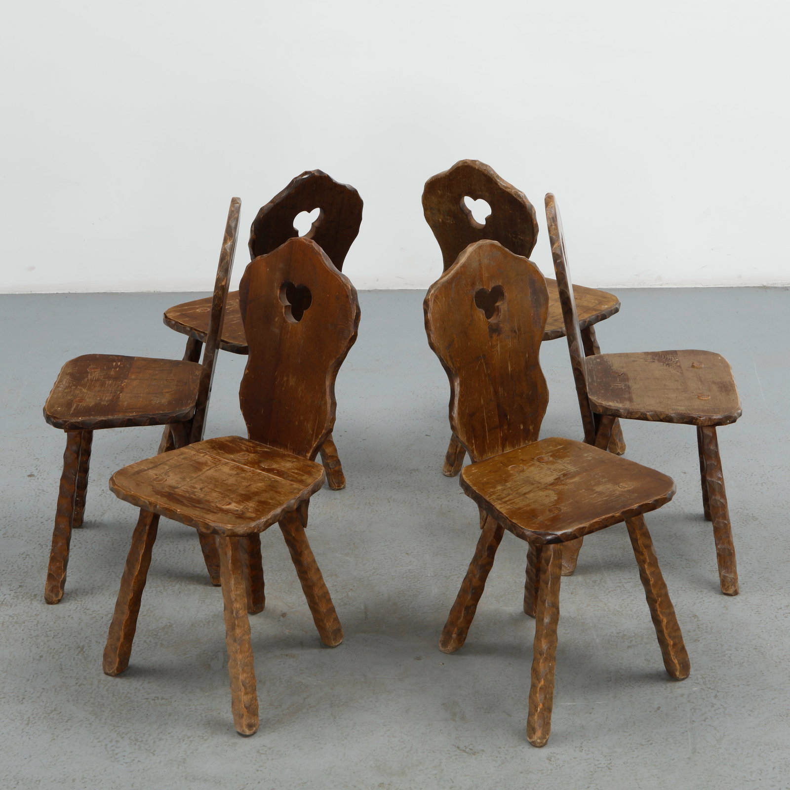 Set of Six Brutalist Spanish Chairs, 1960s: This set of six chairs is hand carved from solid wood, each with a shaped back pierced by a trefoil cutout and raised on faceted, tool textured legs. The rugged, artisan crafted surfaces and warm brow