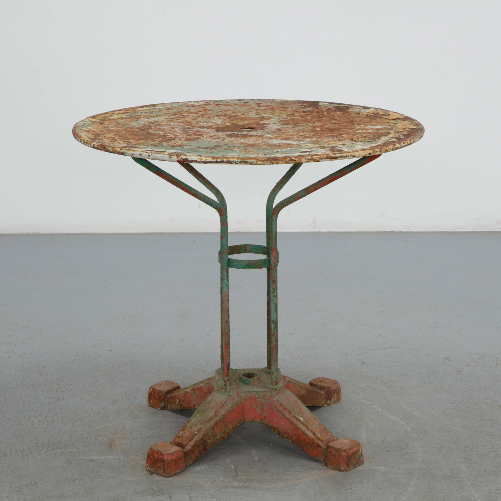 Round Parisian Metal Garden Table, 1950s: Constructed from painted metal, this round garden table is raised on a four legged base with a central umbrella ring. The heavily weathered surface, with losses revealing layers of paint, lends a rich