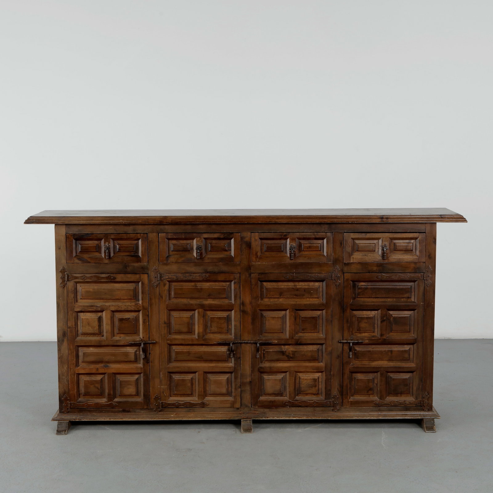 Spanish Carved Solid Sideboard, 1960s: A stained wood sideboard with four paneled doors carved in stepped geometric relief, fitted with hand wrought iron hardware. Dense paneling and dark, richly grained finish typical of Spanish rustic ca