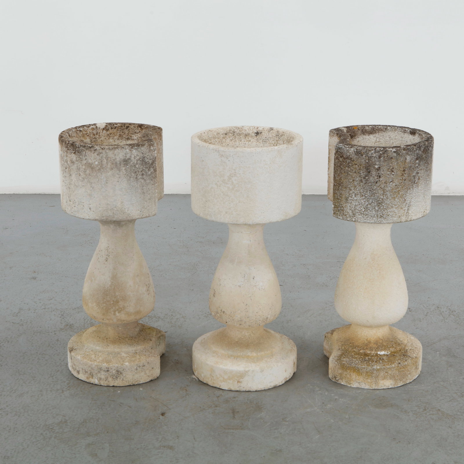 Set of Three Cast Stone Pedestal Planters, Mid-20th Century: Crafted in cast stone, this set of three pedestal planters features a restrained architectural silhouette defined by cylindrical vessels resting on baluster form bases. Their clean proportions and nat