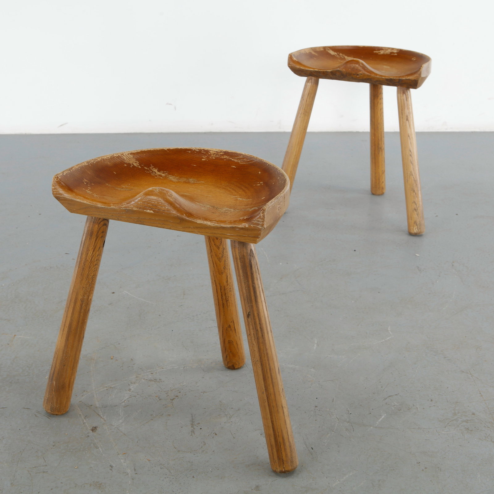 Le Selou, Pair of Brutalist Wood Stools, 1960s: Sculptural pair of solid wood stools by Le Selou, distinguished by deeply hand carved saddle seats and robust splayed legs. Their expressive organic forms and visible craftsmanship embody the rustic e