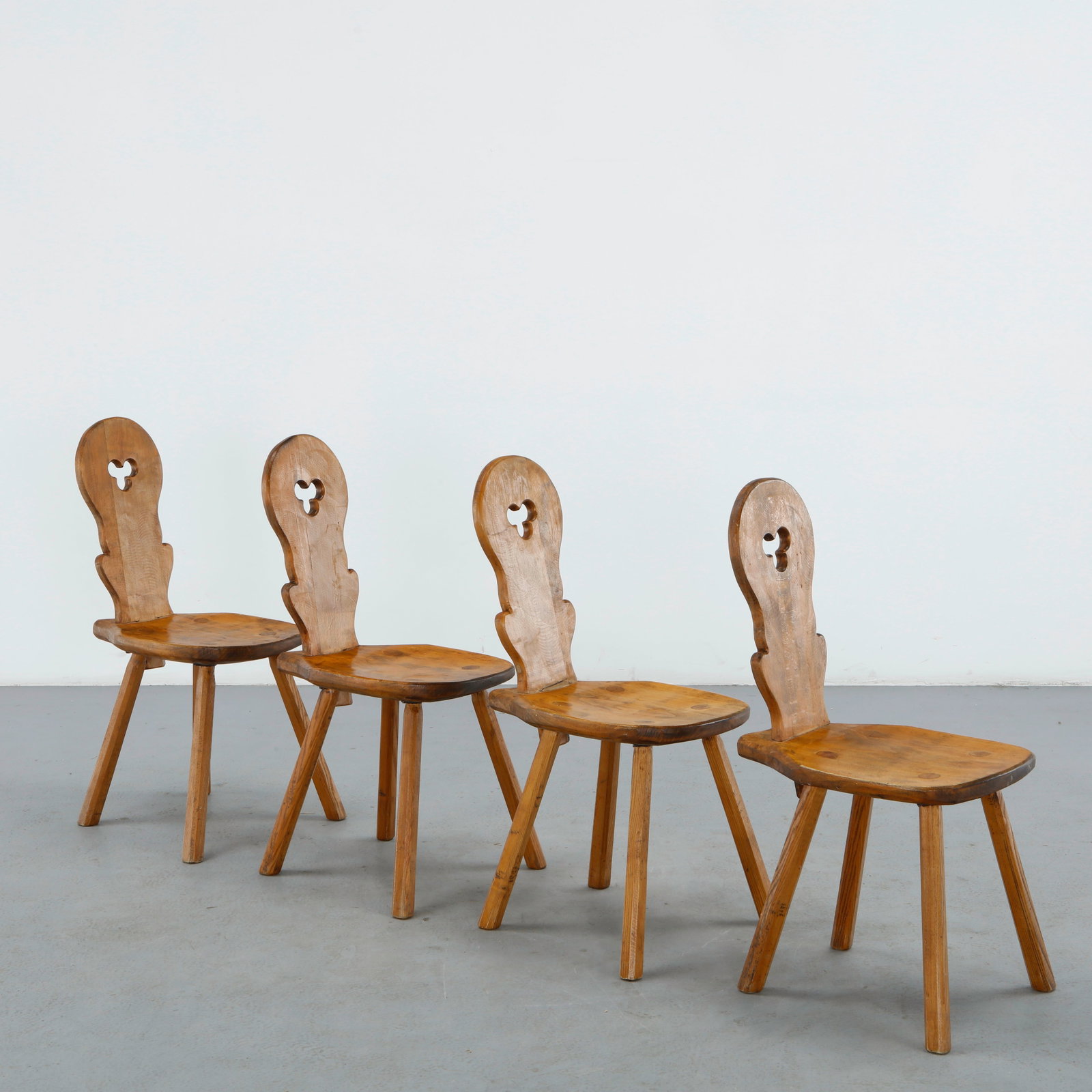 Set of Four French Tiroler Chairs, 1960s: Four Alpine Tiroler chairs with rounded arched backs pierced by a trefoil cutout, solid wood seats, and four splayed legs, a rustic design typical of French mountain chalet furniture. Height: 34.75 in