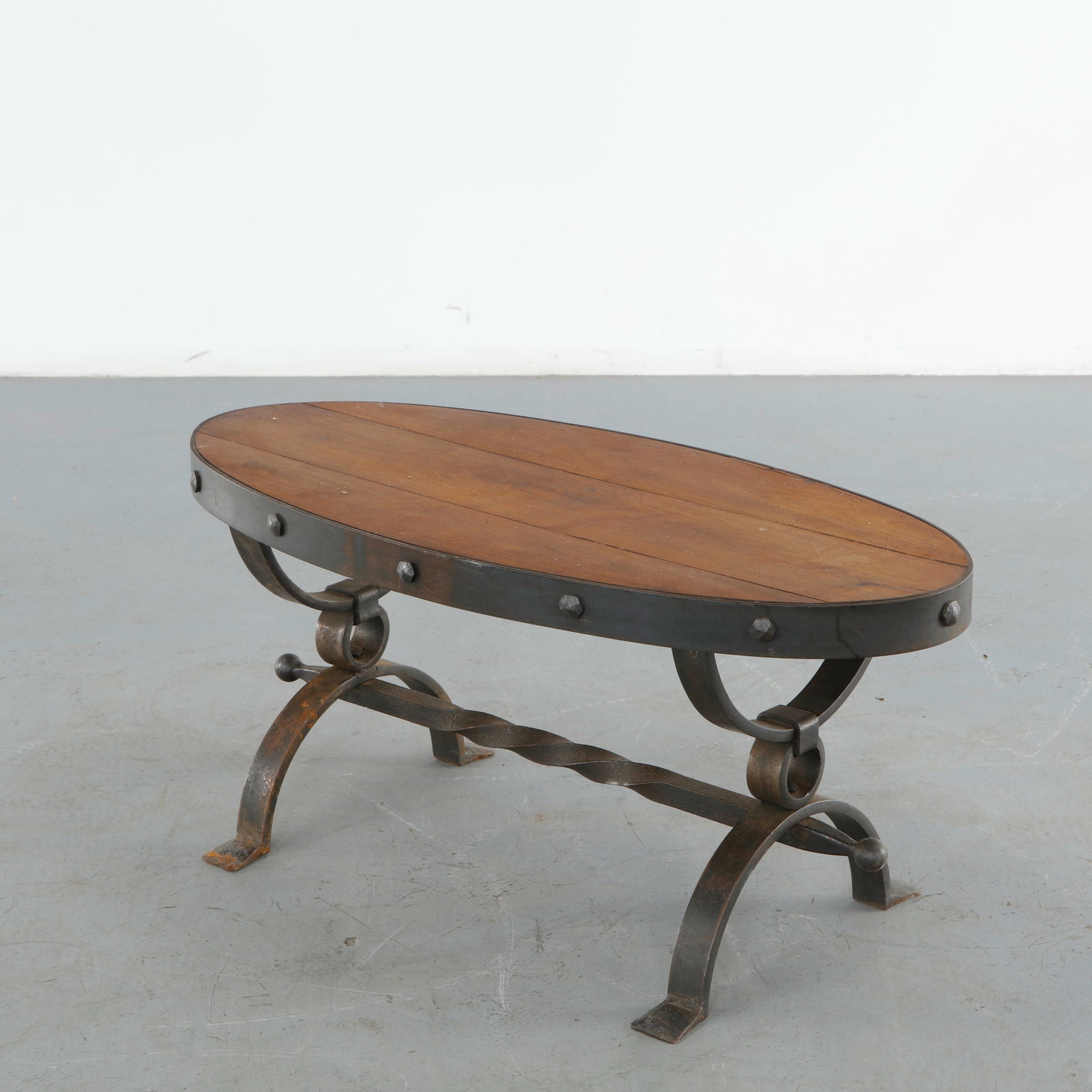 Brutalist Wood and Metal Coffee Table, 1960s: Coffee table featuring an oval solid wood top framed by riveted forged steel and supported by sculptural wrought iron scroll legs joined by a twisted stretcher. A refined Brutalist composition showcas