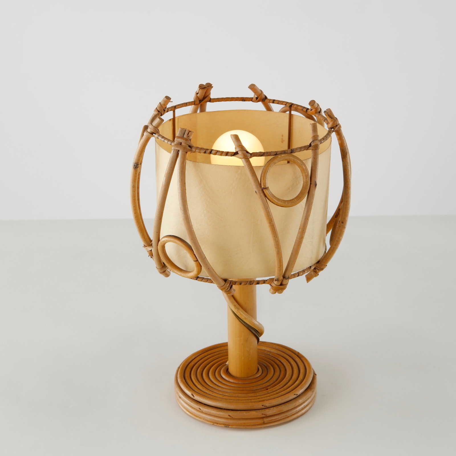 Louis Sognot, Sculptural Rattan Table Lamp, France, 1960s: An expressive table lamp designed by Louis Sognot, featuring a sculptural openwork rattan frame with gracefully curved canes surrounding a parchment diffuser. The organic composition reflects Sognot m