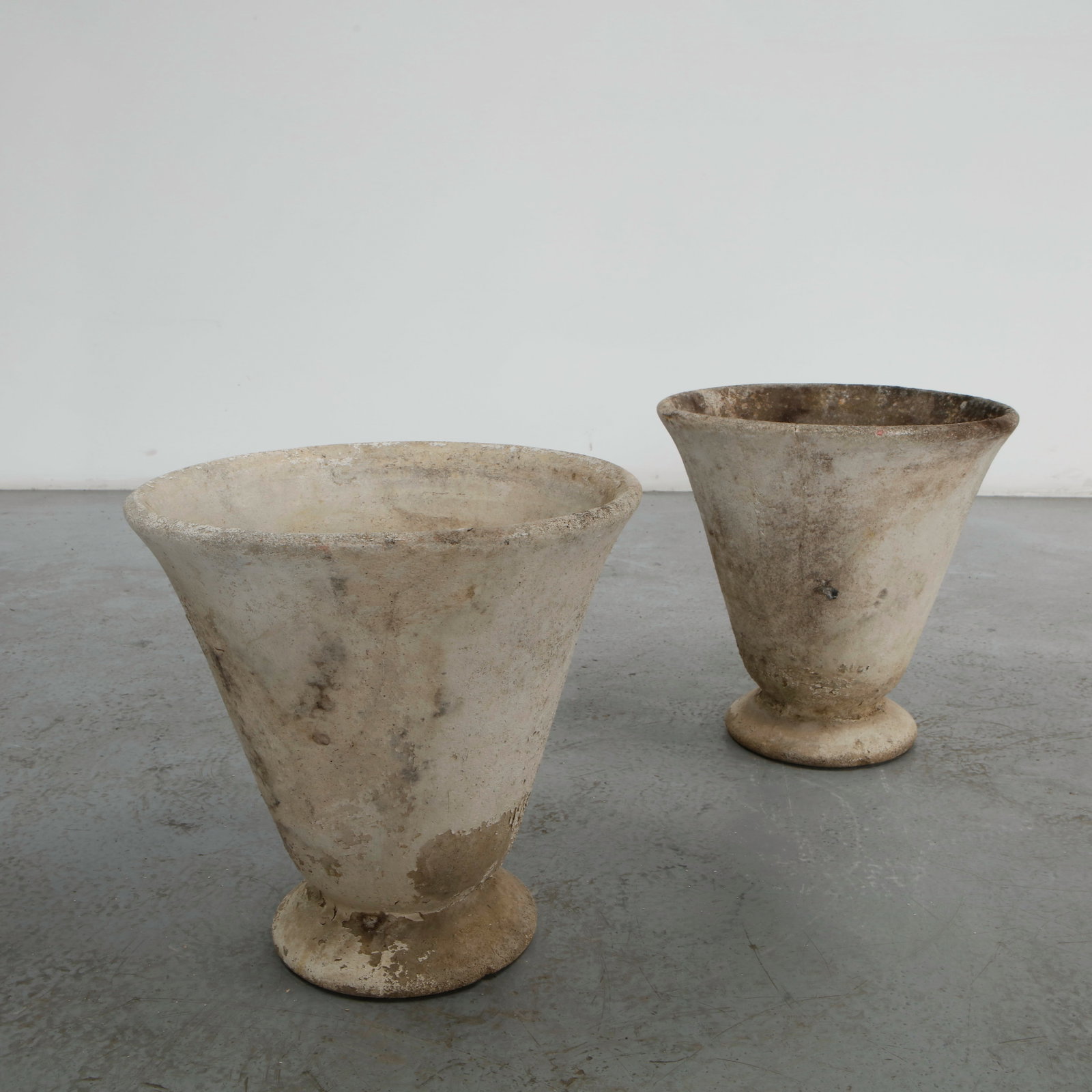 Grandon Fres, Pair of Concrete Planters on Stands, 1960s: A pair of flared urn form planters raised on a round pedestal foot, in cast concrete. Weathered surface, one example retaining a cleaner cream tone, the other with heavier grey patina. Height: 15.25