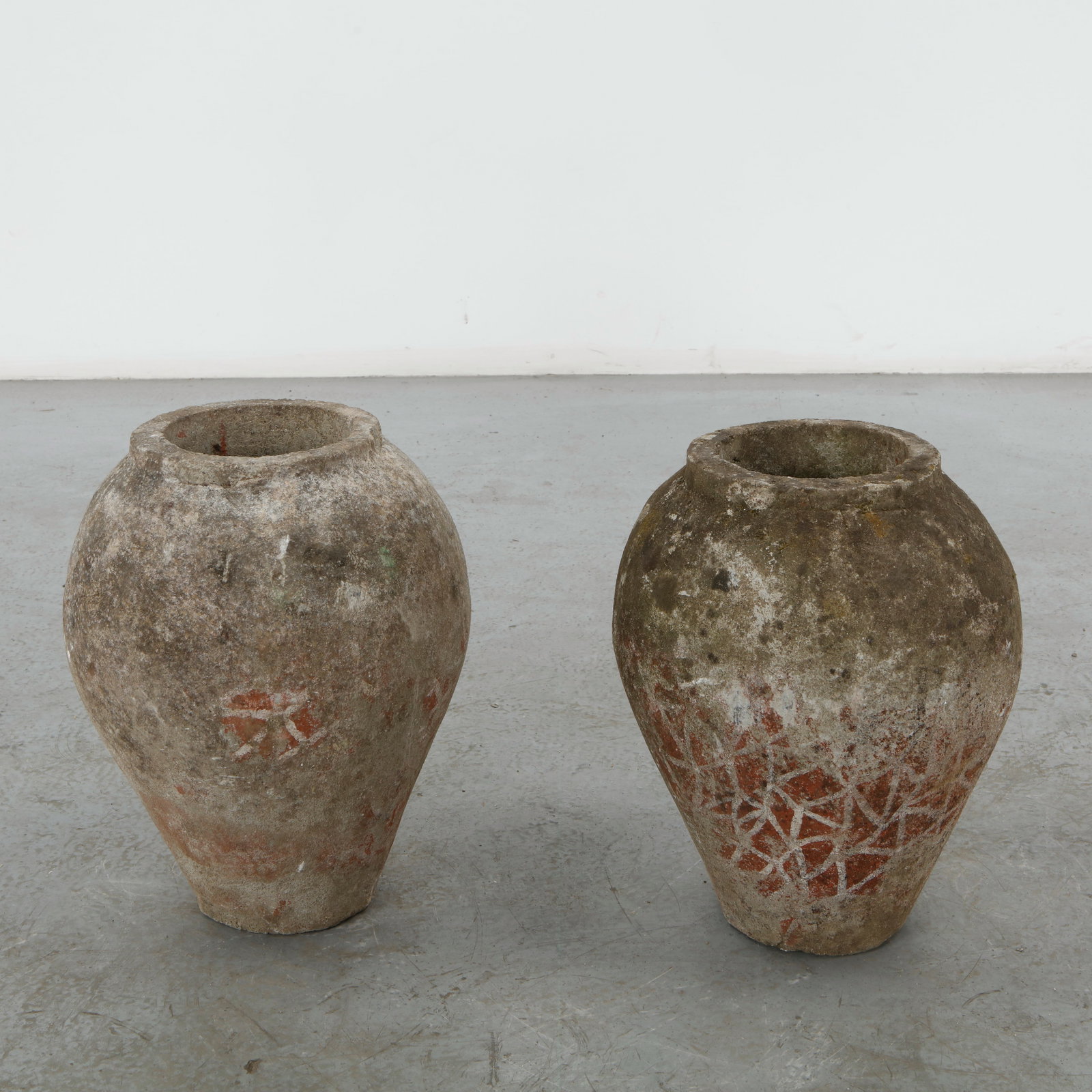 Pair of Urn Concrete Planters, 1960s: A pair of bulbous urn form planters in cast concrete, narrowing to a short neck, retaining traces of a stenciled geometric pattern in orange red beneath a weathered grey surface. Height: 16.25 in. Dia