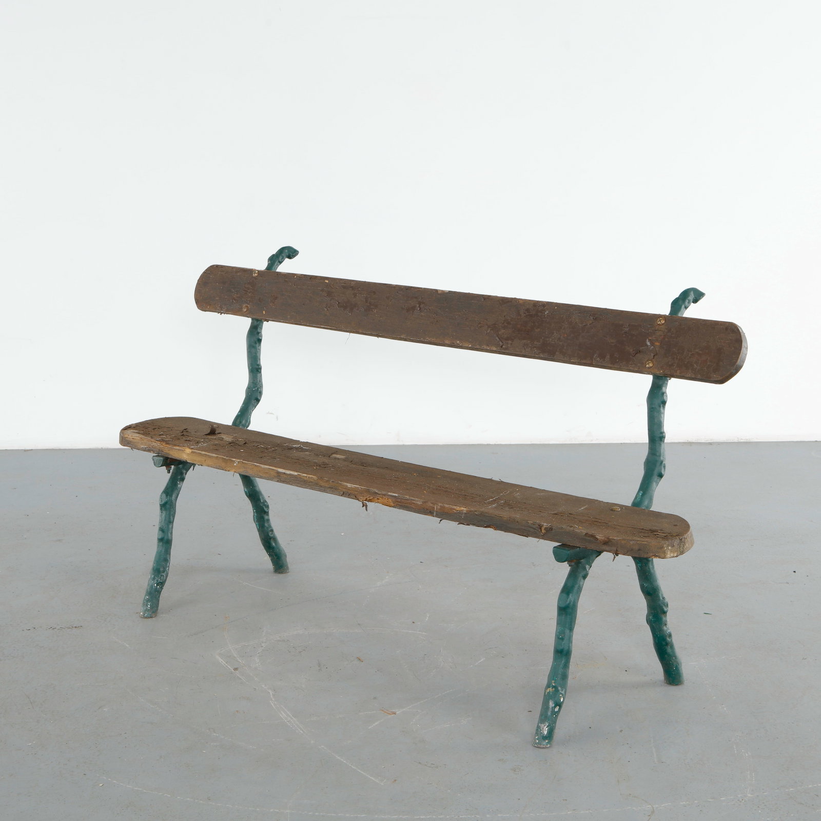 Green Painted Cast Iron Garden Bench, 1950s: This bench features wood slats raised on a cast iron frame with scrolled stretchers and hoof form feet, finished in dark green paint with extensive losses revealing the metal beneath. The sculptural i
