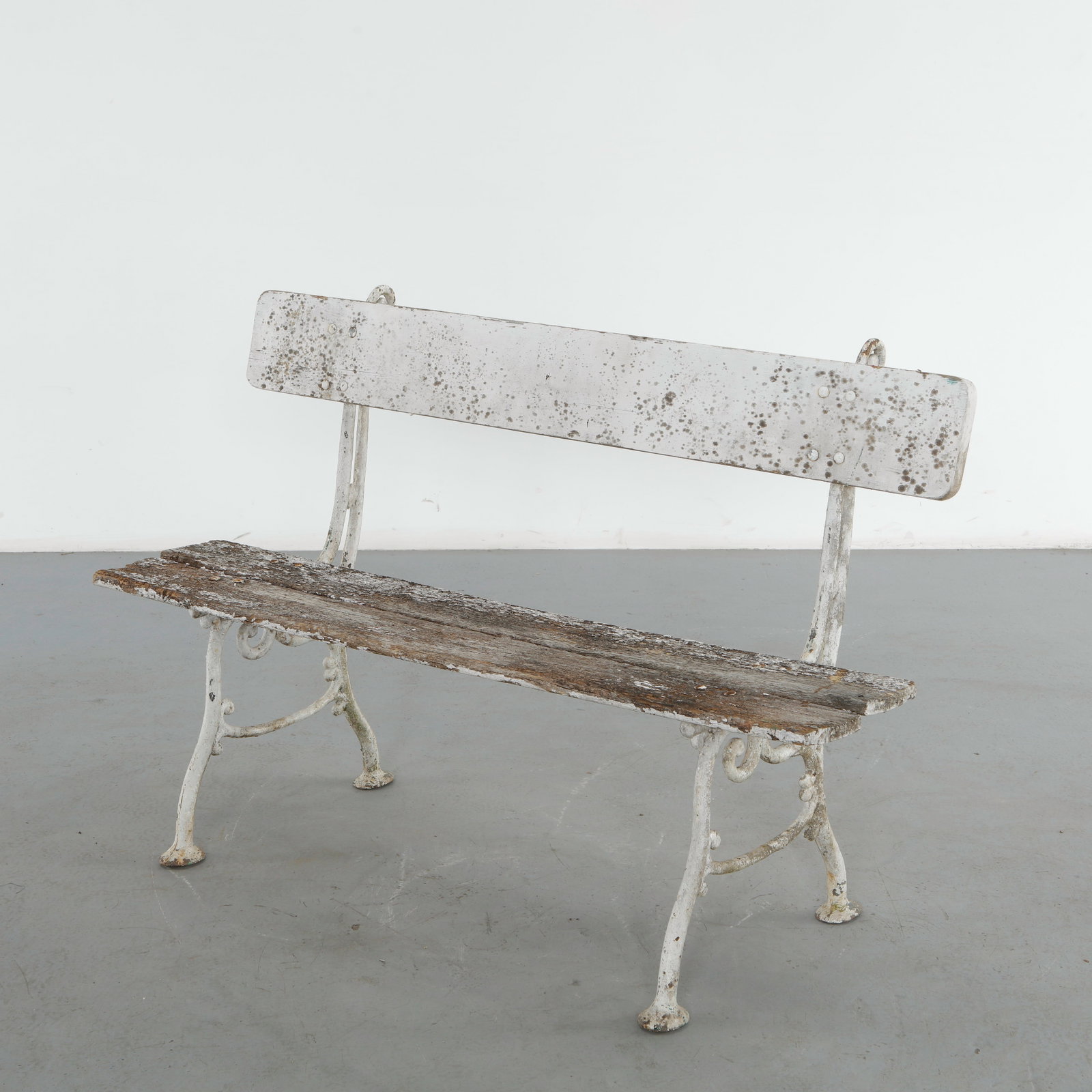 White Painted Wood and Cast Iron Garden Bench, 1950s: Constructed from wood slats set within a scrolled cast iron frame, this bench retains its original white paint, heavily weathered to reveal the bare wood grain beneath. The worn, speckled patina and o