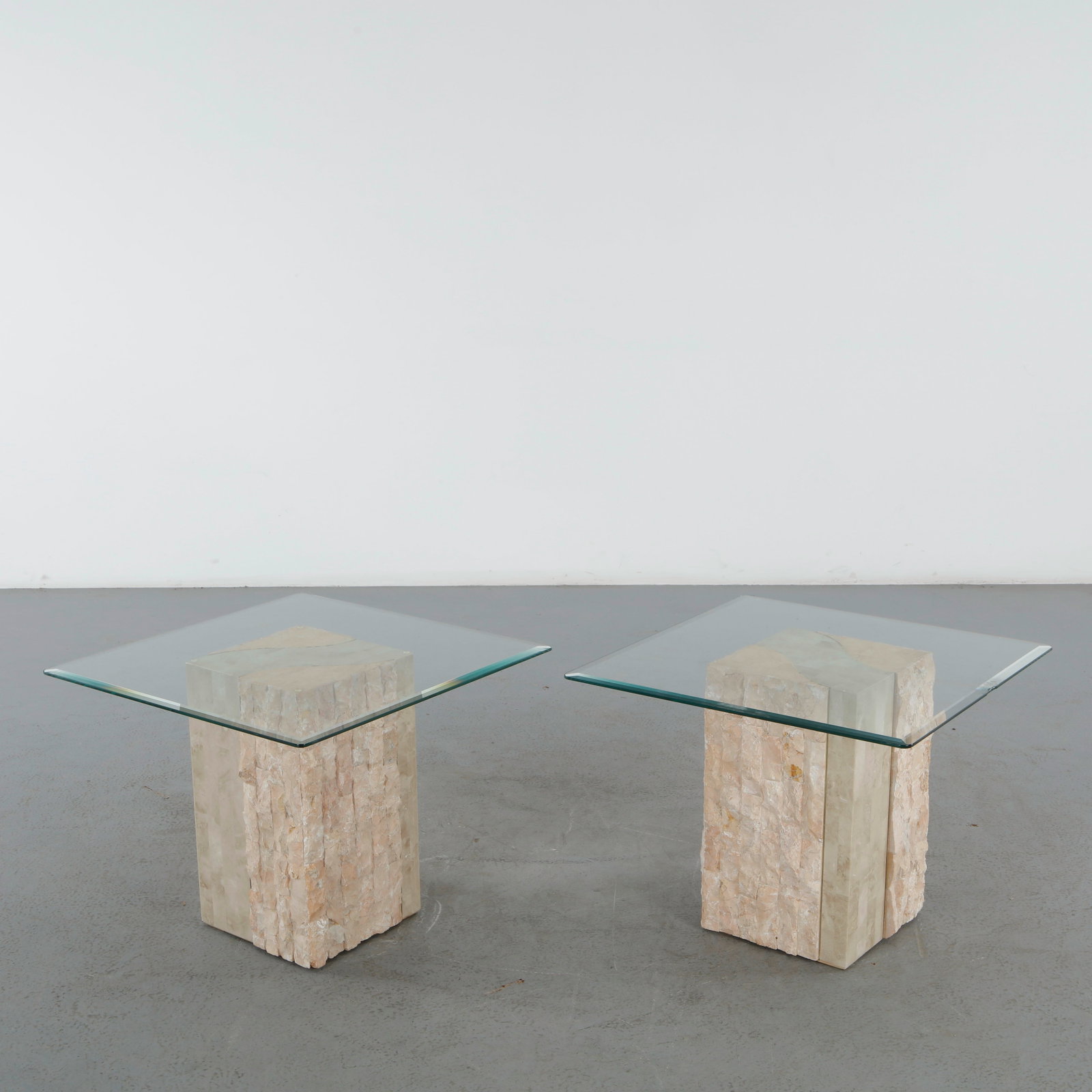 Pair of Glass Side Tables with Travertine Bases: Pair of sculptural side tables featuring square glass tops supported by carved travertine bases. Their geometric form and natural stone texture embody the refined aesthetic of 1980s design. Height: 20