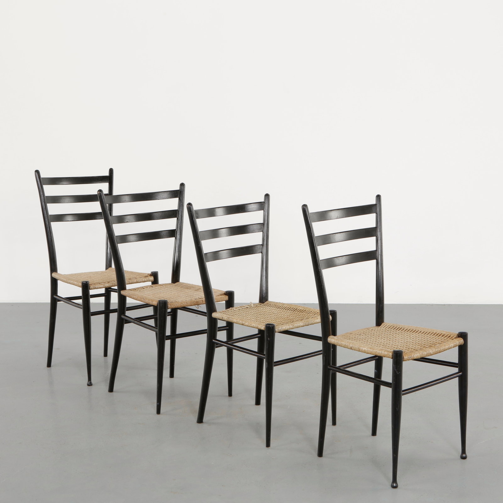 Set of Four Rope and Black Laquered Wood Chairs in the style of Gio Ponti, 1960s: Executed in black lacquered wood with slender tapered legs and graphic ladder backrests. The woven rope seats introduce a natural counterpoint to the dark linear structure. A refined dining set