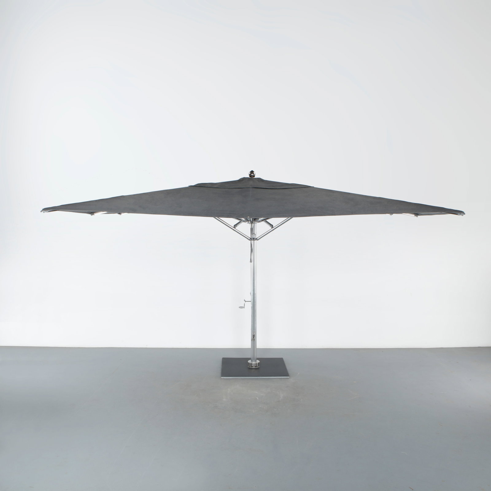 Tuuci, Ocean Master Max Cantilever Umbrella: A large offset patio umbrella in brushed stainless steel, its square gray canopy suspended from a cantilevered arm on a heavy square base, operated by a hand crank and fitted with a locking rotation m