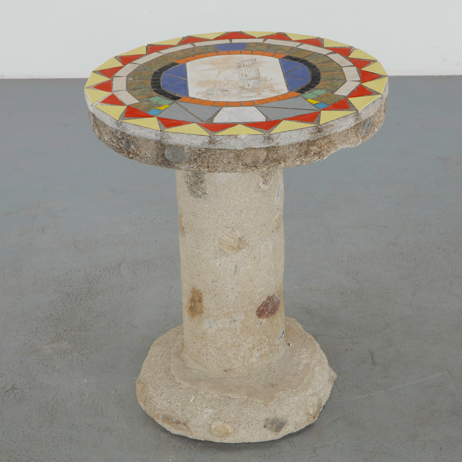 Mosaic Stone Pedestal Table, 1960s: Decorative pedestal table executed in stone and aggregate concrete, featuring a vibrant geometric mosaic top centered by a delicate pastoral scene. The cylindrical base and exposed stone inclusions le