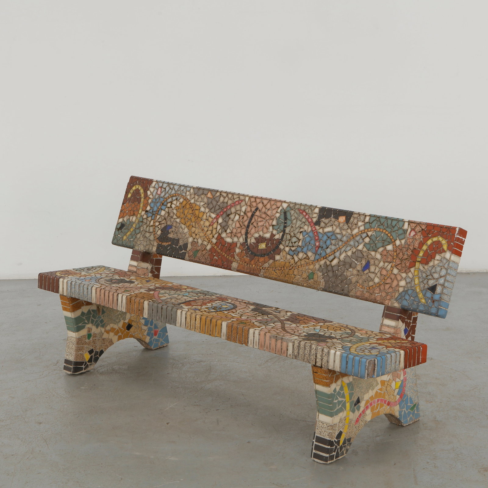 Mosaic Bench with Abstract Motif, 1960s: A monumental outdoor bench entirely clad in hand-set mosaic fragments, animated by an abstract serpentine motif in muted earth tones, blue and red. The richly textured surface and sculptural concrete 