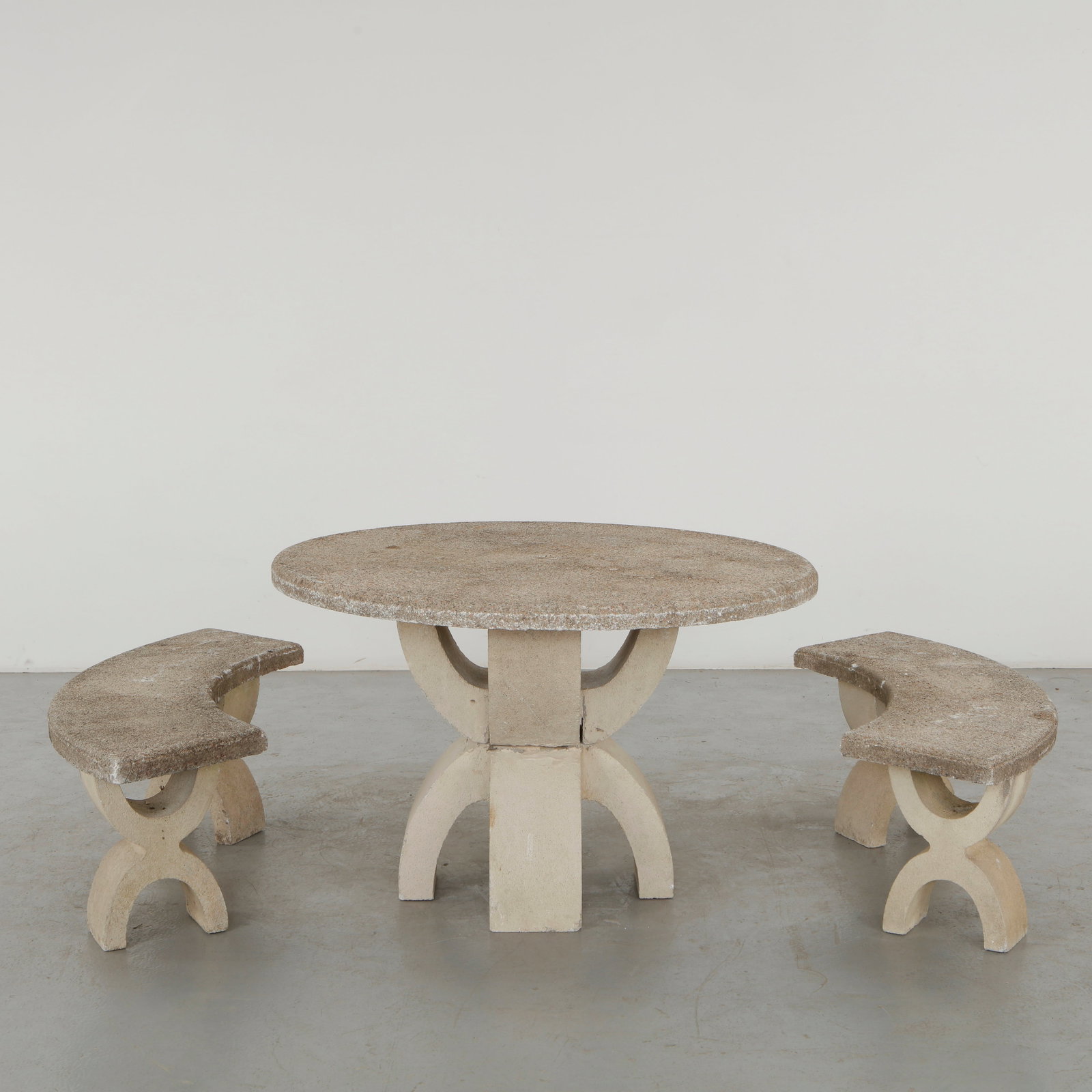 Sculptural Stone Outdoor Dining Set, 1960s: A monumental outdoor dining ensemble comprising a circular stone table and two opposing crescent-shaped benches. Characterized by boldly sculptural supports and a restrained mineral palette, the set p