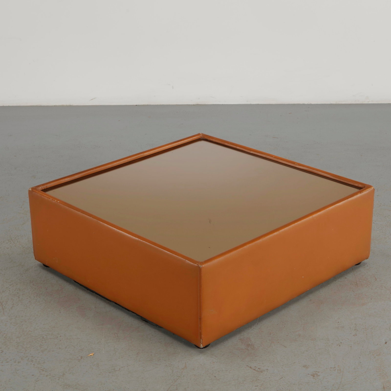 Roche Bobois, Leather Wrapped Glass Coffee Table, 1970s: A refined coffee table featuring a substantial square glass top enclosed within a warm cognac leather-clad frame. The restrained geometry and richly colored upholstery exemplify the sophisticated