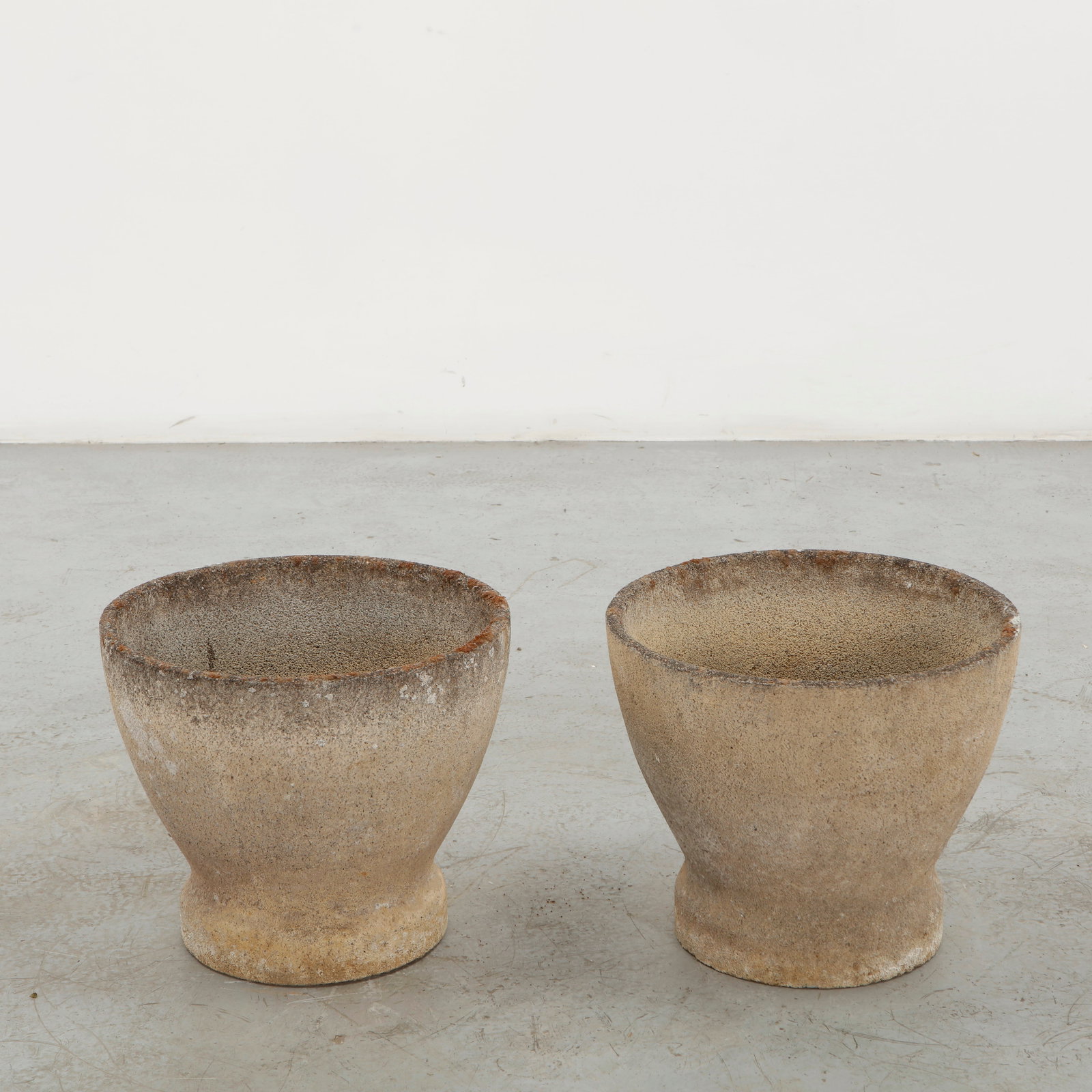 Pair of Cast Stone Round Planters, 1960s: A refined pair of cast stone planters featuring gently tapering, rounded bodies raised on compact circular footings. The granular surface and richly weathered patina lend the vessels a restrained scul